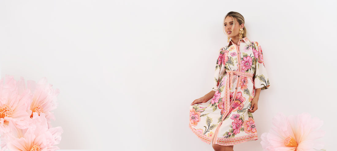 minnie + MAXXIE Lea Pink Floral Dress with gold event earrings, surrounded by pink paper flowers