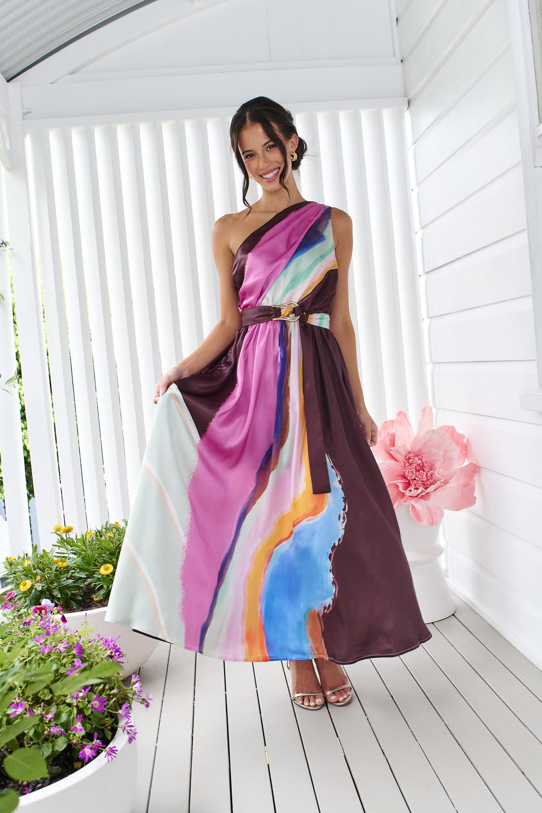 Woman wearing the minnie + MAXXIE Alessandra One Shoulder Maxi Dress with a graphic abstract print and matching waist tie.