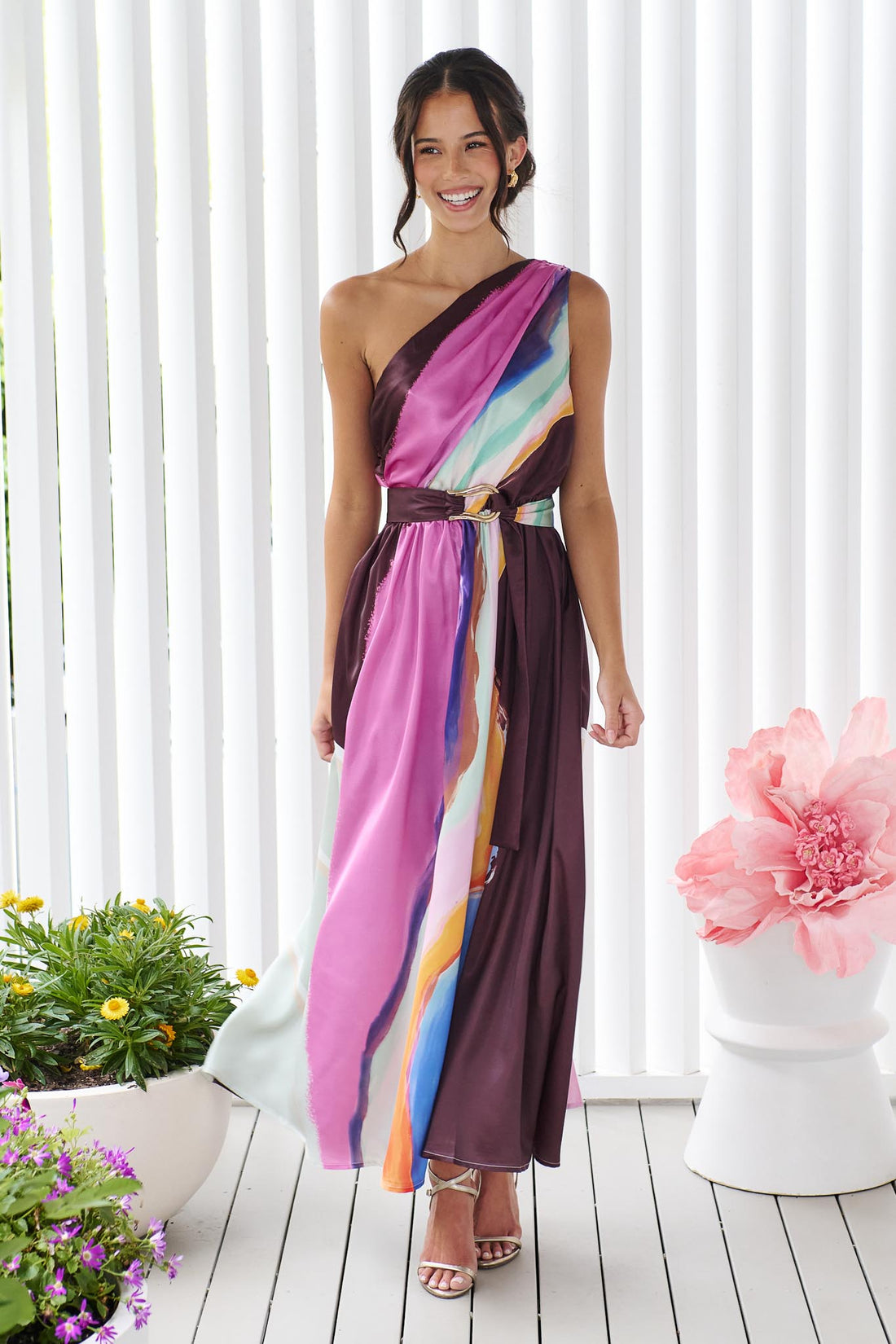 Woman wearing the minnie + MAXXIE Alessandra One Shoulder Maxi Dress with a graphic abstract print and matching waist tie.