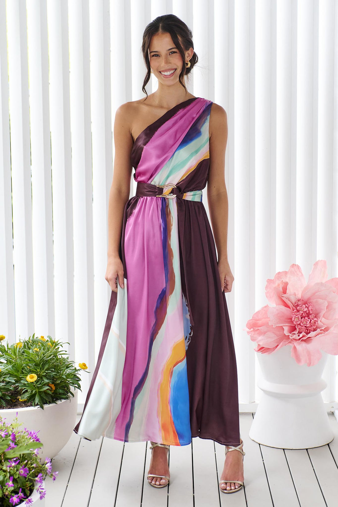 Woman wearing the minnie + MAXXIE Alessandra One Shoulder Maxi Dress with a graphic abstract print and matching waist tie.