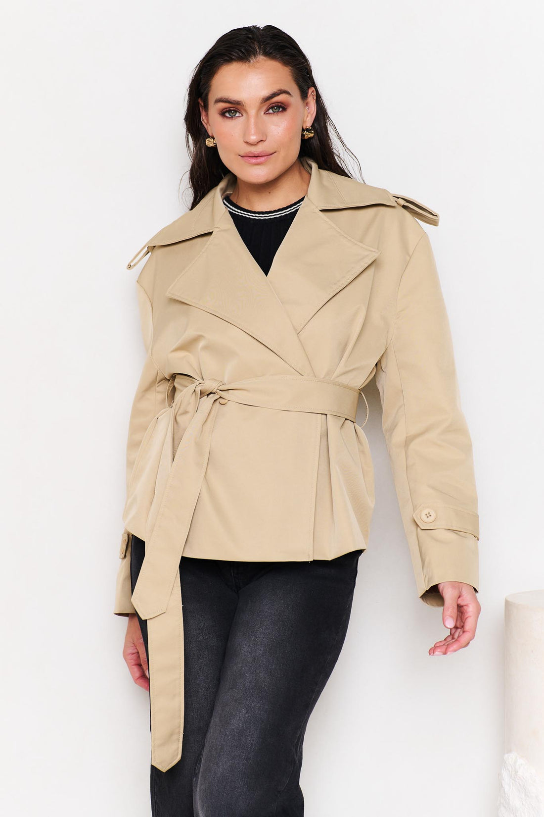 Woman wearing a minnie + MAXXIE beige cropped trench coat with black denim jeans
