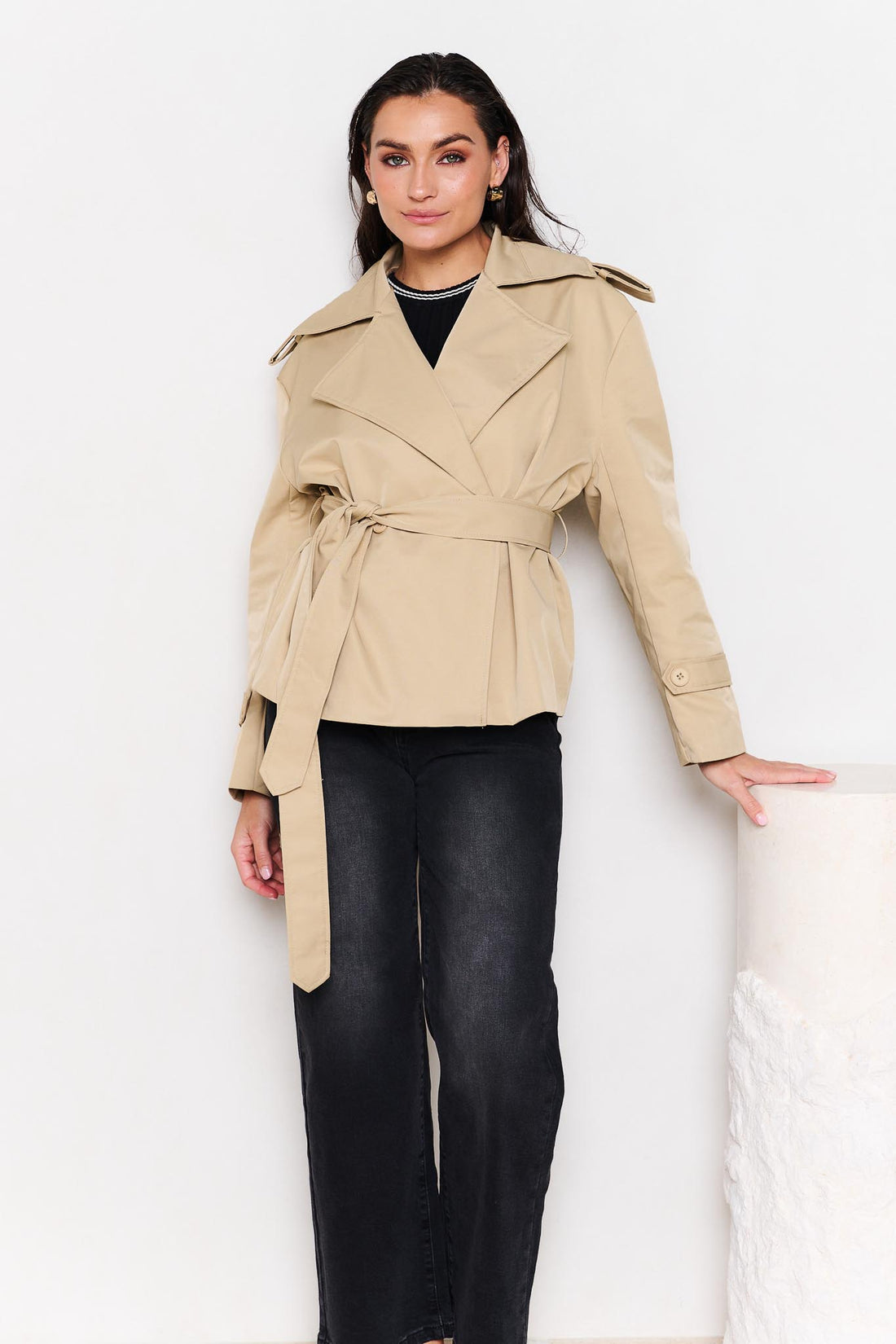 Woman wearing a minnie + MAXXIE beige cropped trench coat with black denim jeans