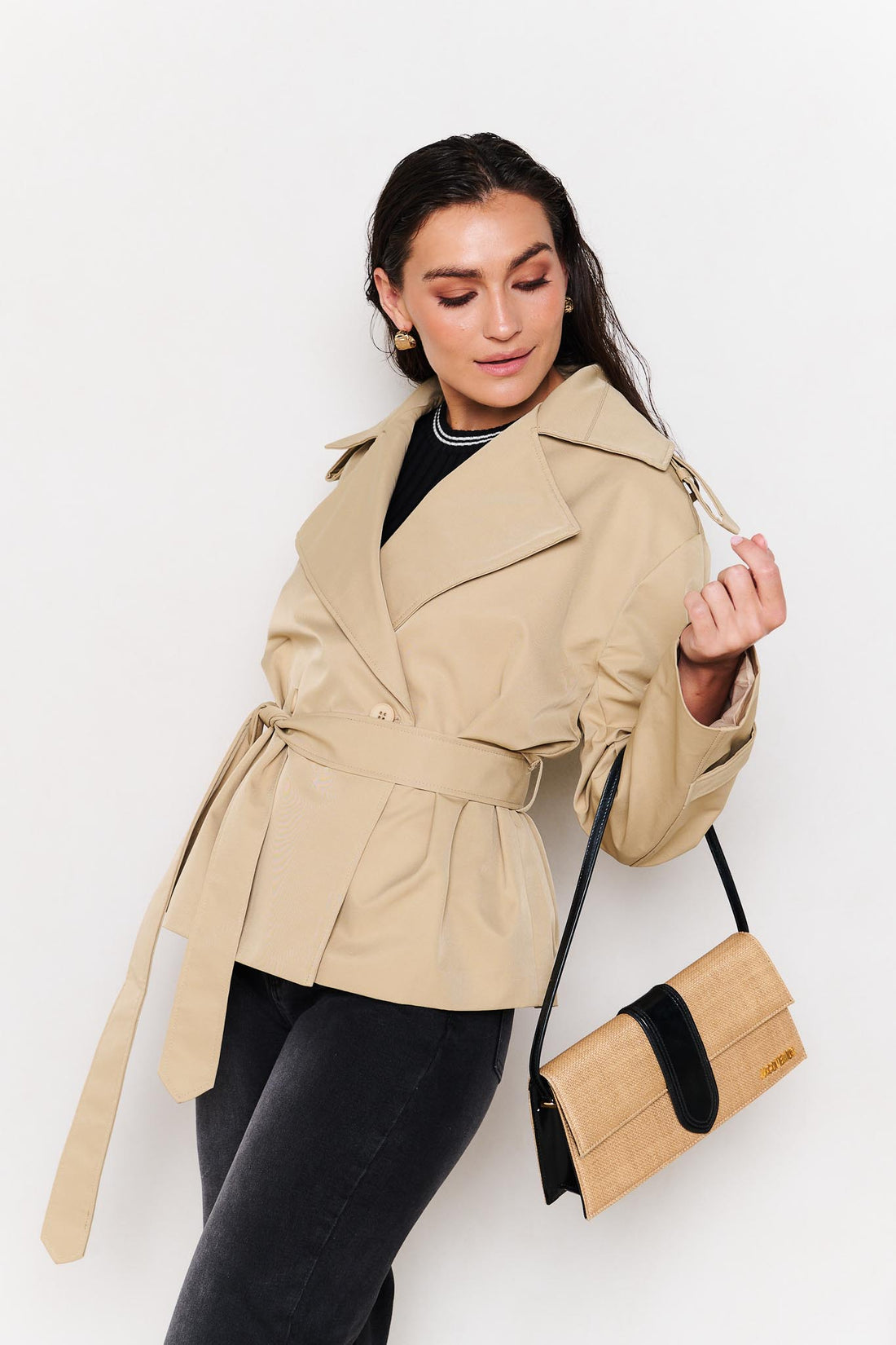 Woman wearing a minnie + MAXXIE beige cropped trench coat with a Jacquemus handbag