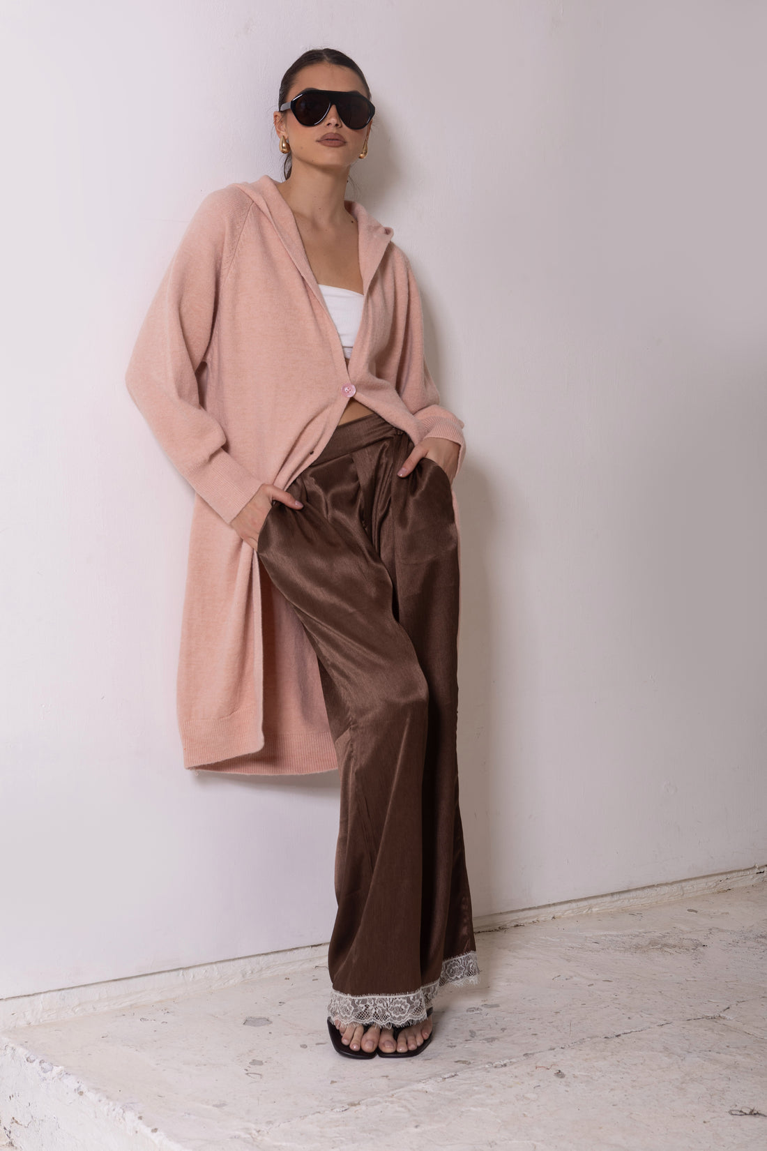 Woman wearing minnie + MAXXIE Lennox longline hooded cardi with brown satin pants in a white room