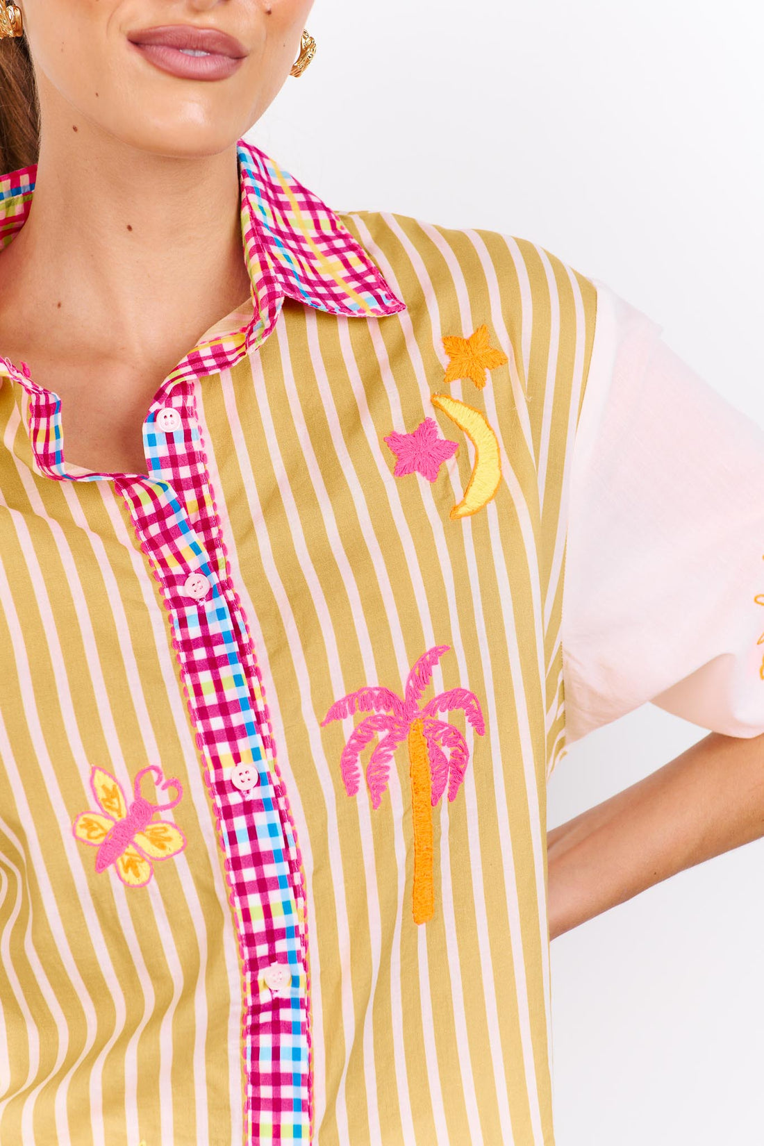 Detail of the minnie + MAXXIE Ciao Bella Cotton Shirt with a tan and white stripe print, gingham trims and neon embroidered motifs.