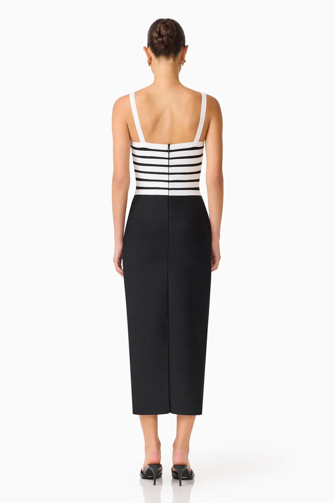 Back view of a model wearing the ELLIATT Ninette Column Midi Dress in Black & White with a white criss-cross strap pattern across the bodice, photographed against a plain white studio background.