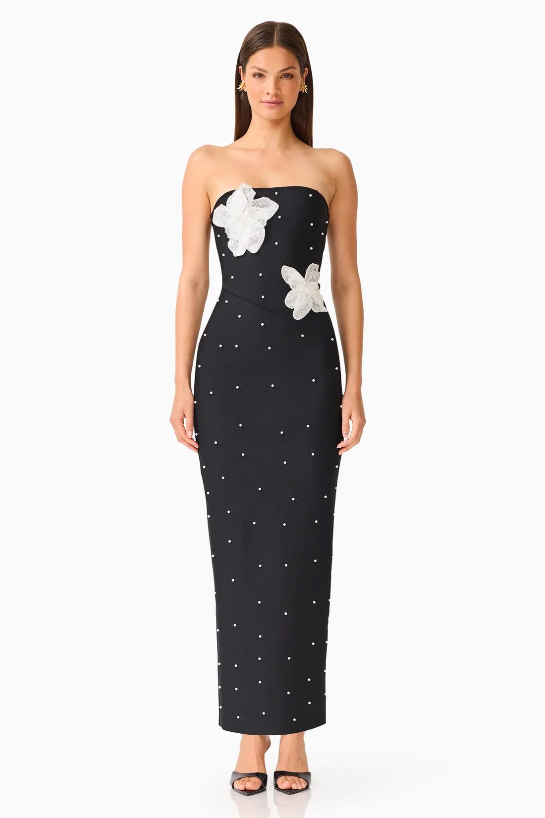 A woman modelling the ELLIATT Natasia embellished strapless black maxi dress with white floral appliqué flowers and pearl stud embellishments, photographed against a plain white studio background.