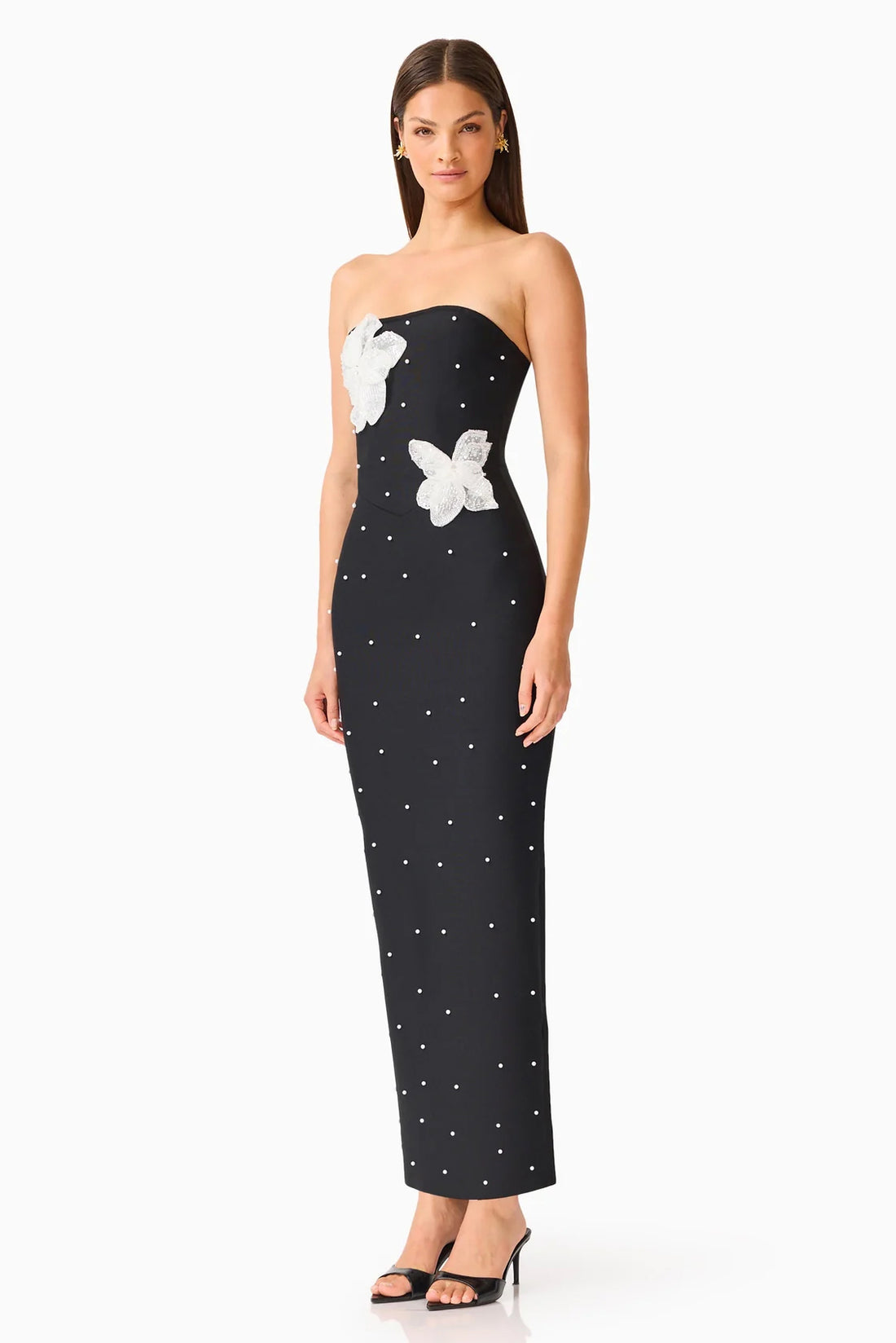 A woman modelling the ELLIATT Natasia embellished strapless black maxi dress with white floral appliqué flowers and pearl stud embellishments, photographed against a plain white studio background.
