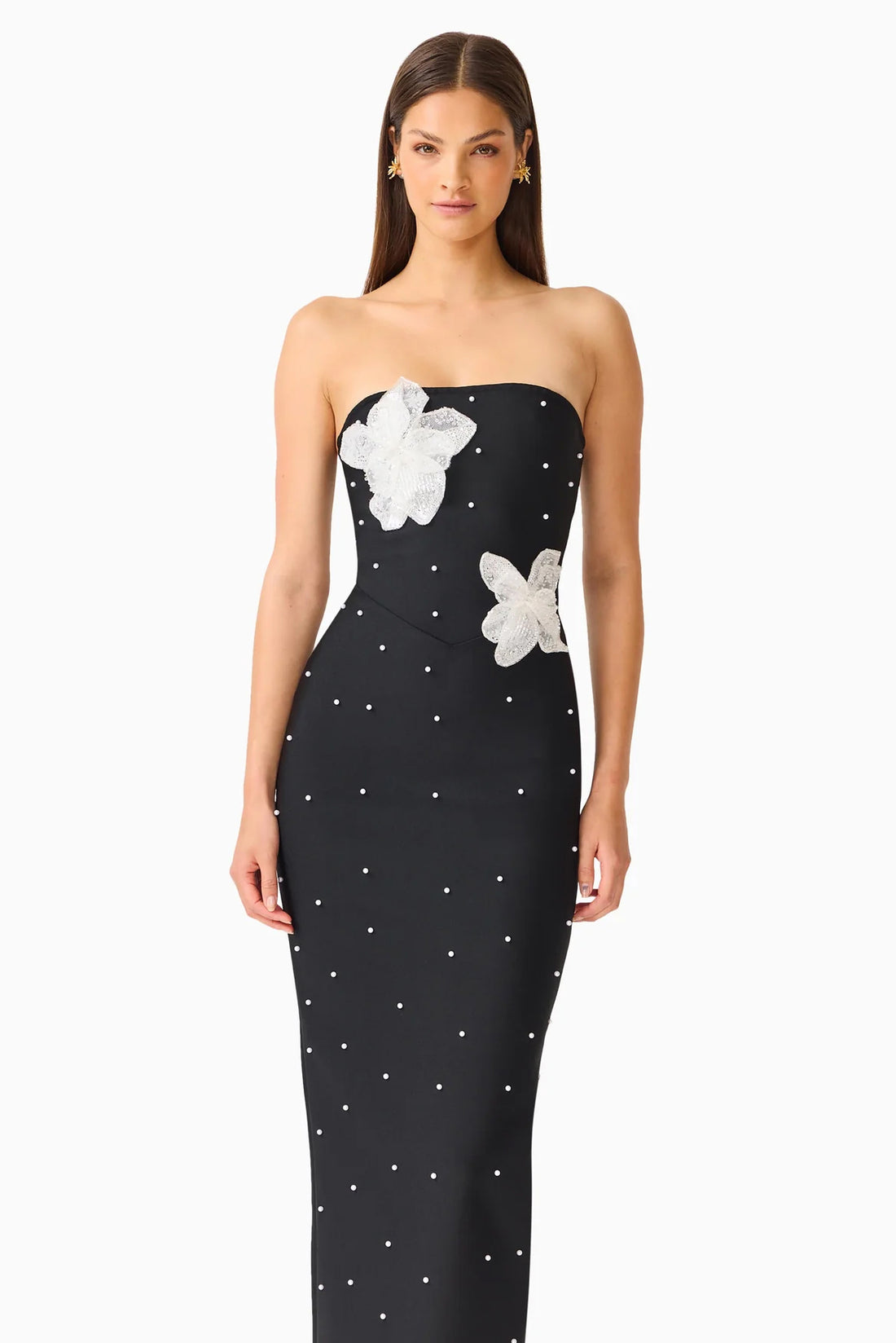 A woman modelling the ELLIATT Natasia embellished strapless black maxi dress with white floral appliqué flowers and pearl stud embellishments, photographed against a plain white studio background.