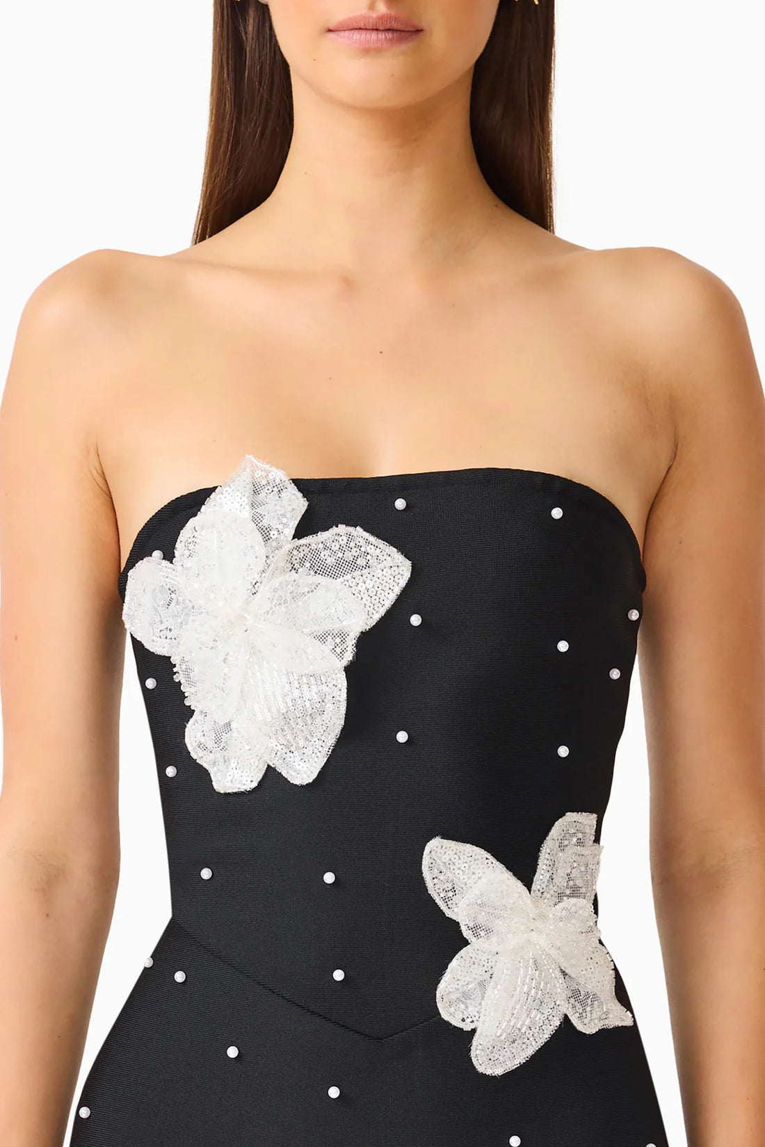 Detail of a woman modelling the ELLIATT Natasia embellished strapless black maxi dress with white floral appliqué flowers and pearl stud embellishments.