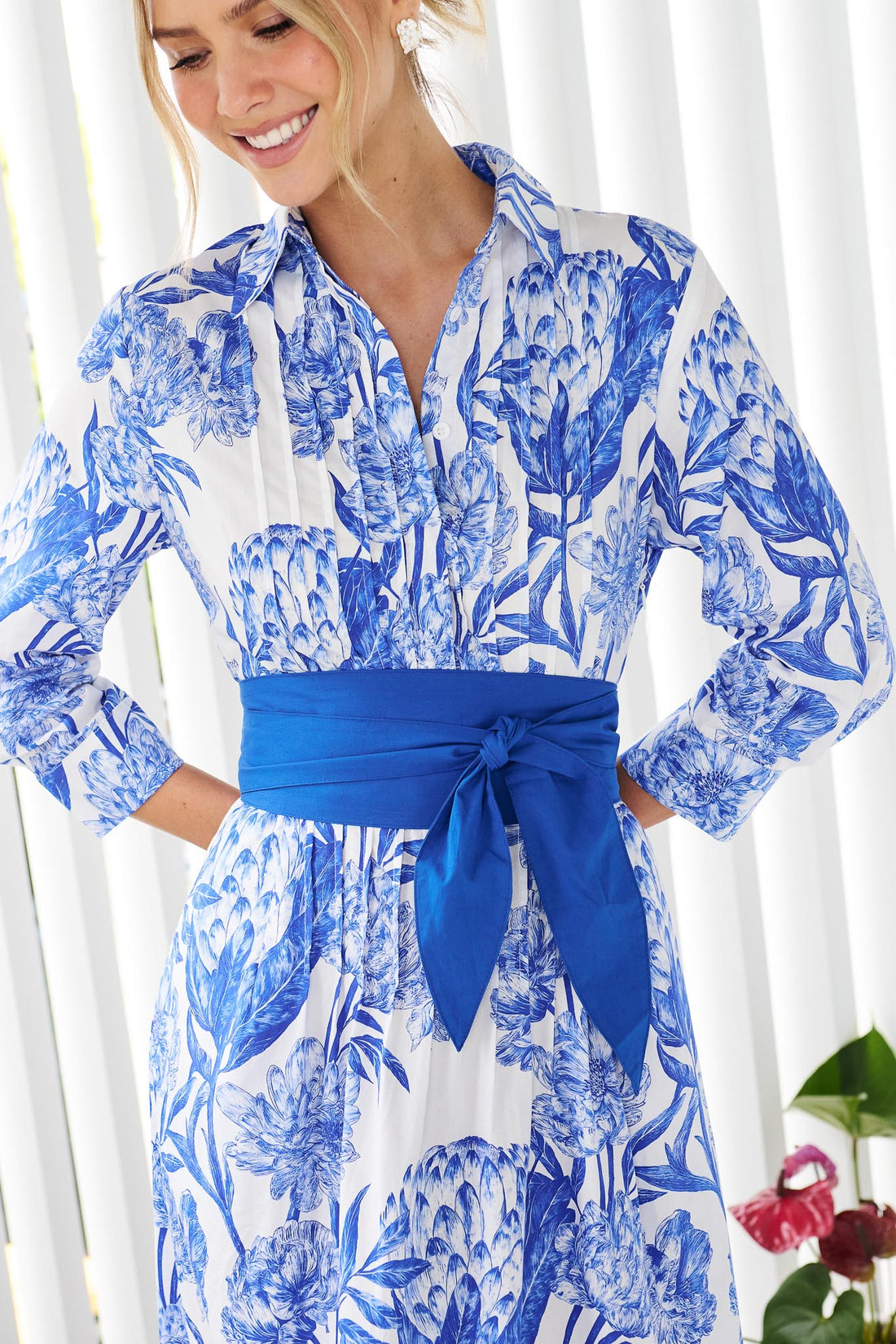 Detail of a woman wearing the minnie + MAXXIE Helena cotton midi dress with a blue floral print, pintuck pleats and a matching blue sash waist tie.