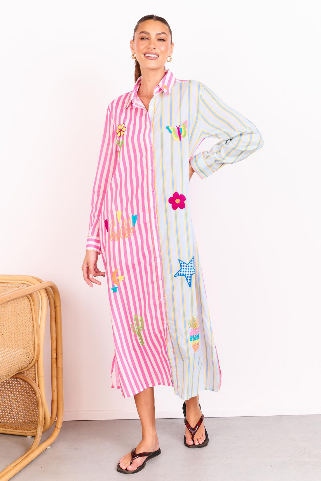 Woman wearing the minnie + MAXXIE Hello Sunshine Cotton midi shirt dress with long sleeves. One side is pink stripes and the other side blue pinstripes. She is standing in front of a white wall.