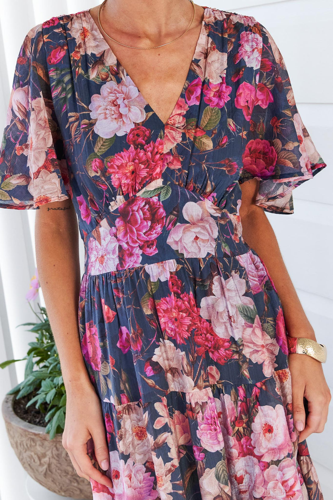 Close up of a woman wearing the short-sleeve, V-neck minnie + MAXXIE Hollie maxi dress with a rose print on a dark navy background.