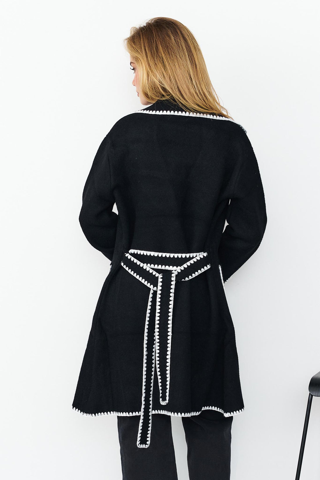 Back view of woman wearing minnie + MAXXIE wool blend black Kinsey jacket with white blanket stitch trim, a white top, and washed black denim jeans.