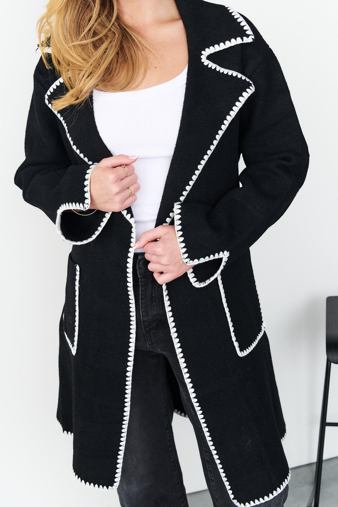 Detail of woman wearing minnie + MAXXIE wool blend black Kinsey jacket with white blanket stitch trim, a white top.
