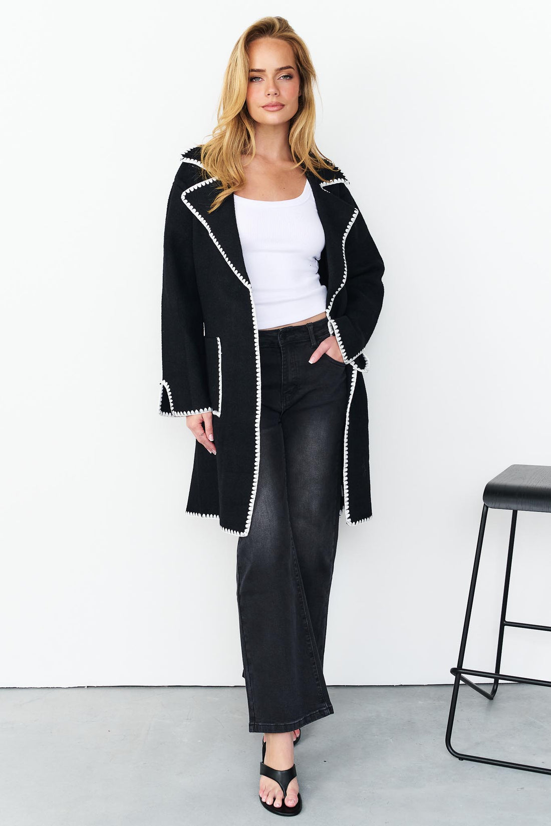 Woman wearing minnie + MAXXIE wool blend black Kinsey jacket with white blanket stitch trim, a white top, and washed black denim jeans.