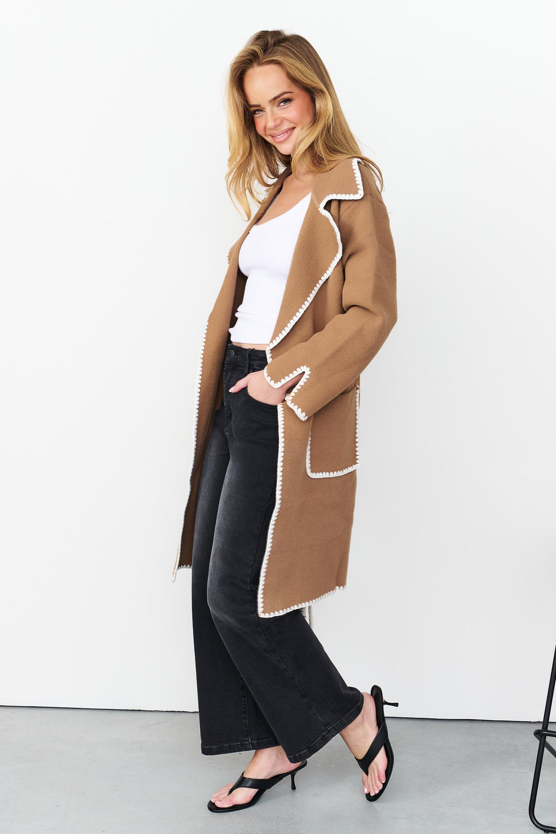 Side view of woman wearing minnie + MAXXIE wool blend Kinsey jacket in pecan with white blanket stitch trim and washed black denim jeans.