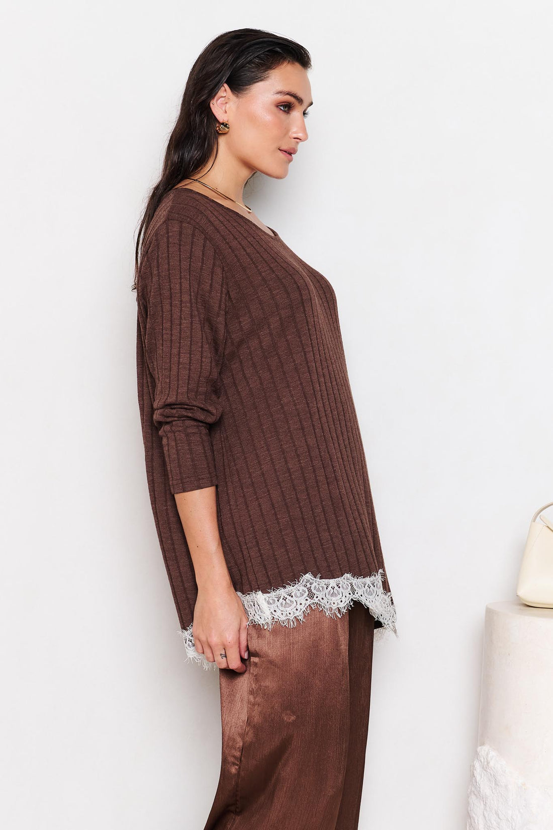 Woman wearing a brown ribbed sweater with lace trim and matching pants against a white background