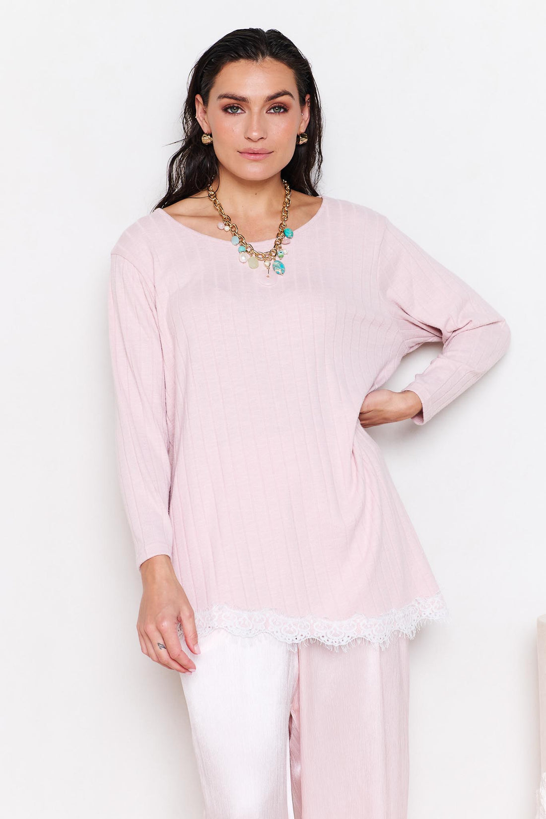 Woman wearing a light pink long-sleeve top with lace trim and a necklace against a white background
