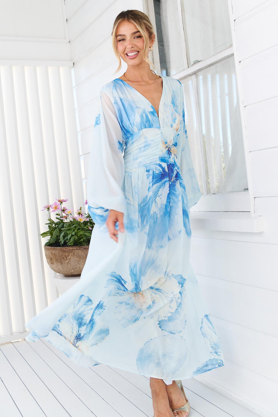 A woman wearing the minnie + MAXXIE Lola long-sleeve v-neck maxi dress with a blue watercolor floral print.