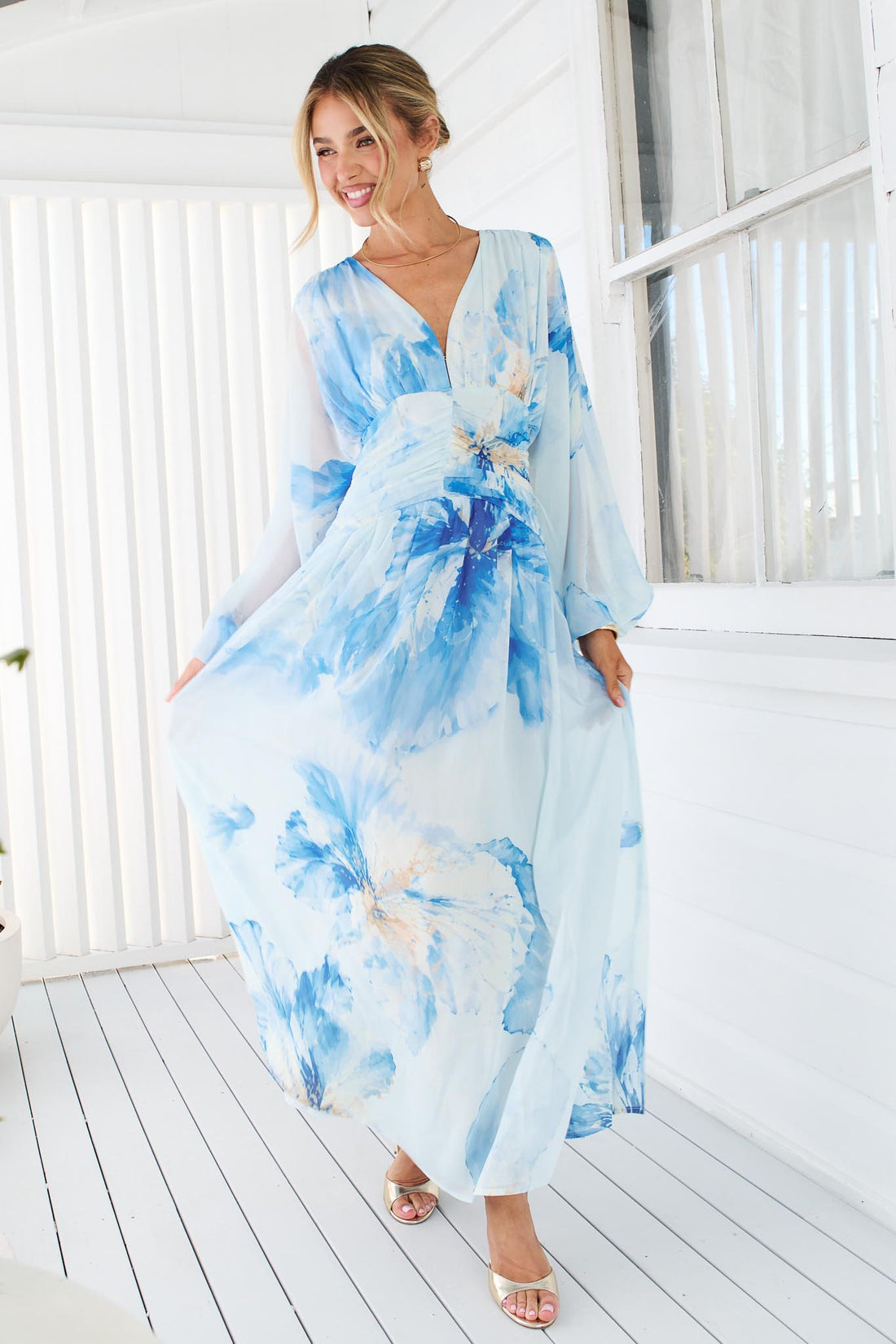 A woman wearing the minnie + MAXXIE Lola long-sleeve v-neck maxi dress with a blue watercolor floral print.