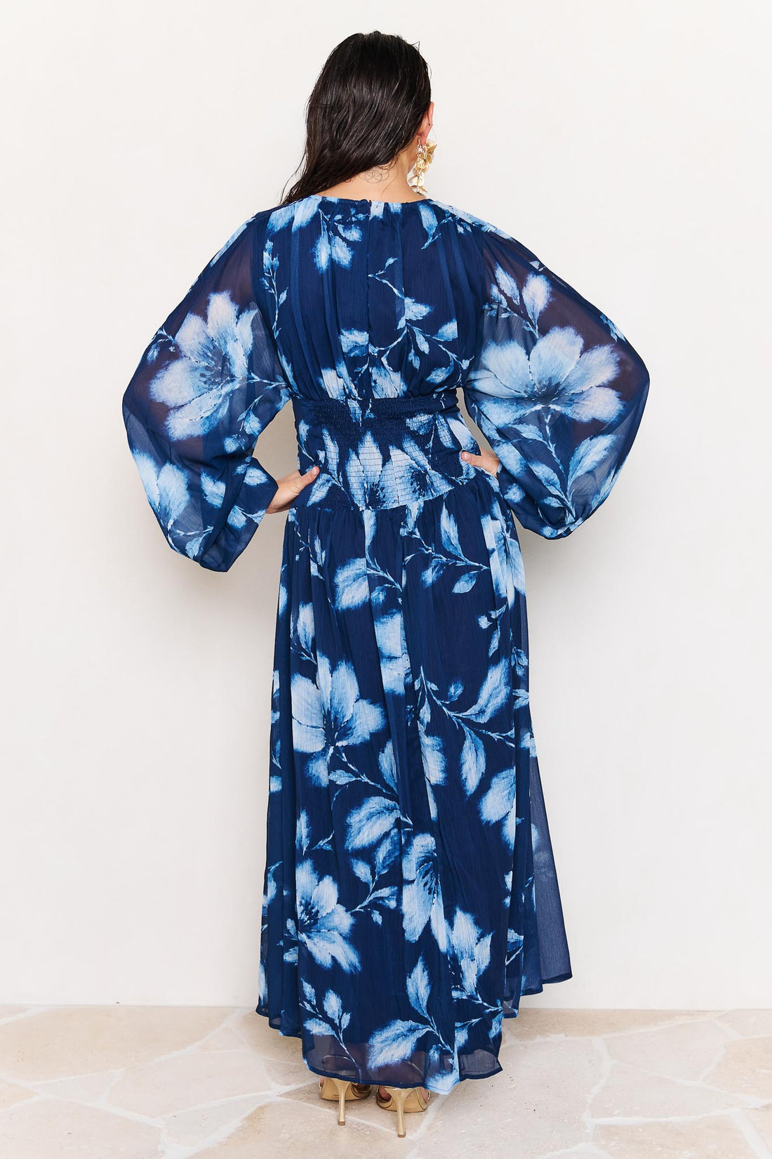 Back view of woman wearing the minnie + MAXXIE Lola blue floral event dress on a white background