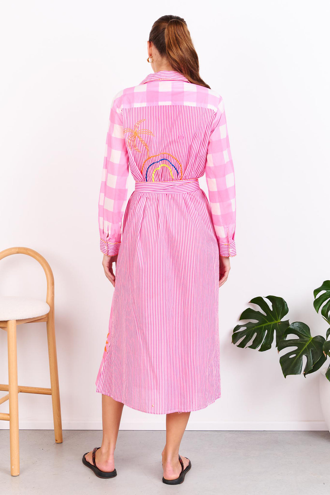Back view of a woman wearing the minnie + MAXXIE Lovely Day Cotton midi shirt dress with long sleeves and a pink stripe and gingham print with neon embroidery and a matching waist tie.