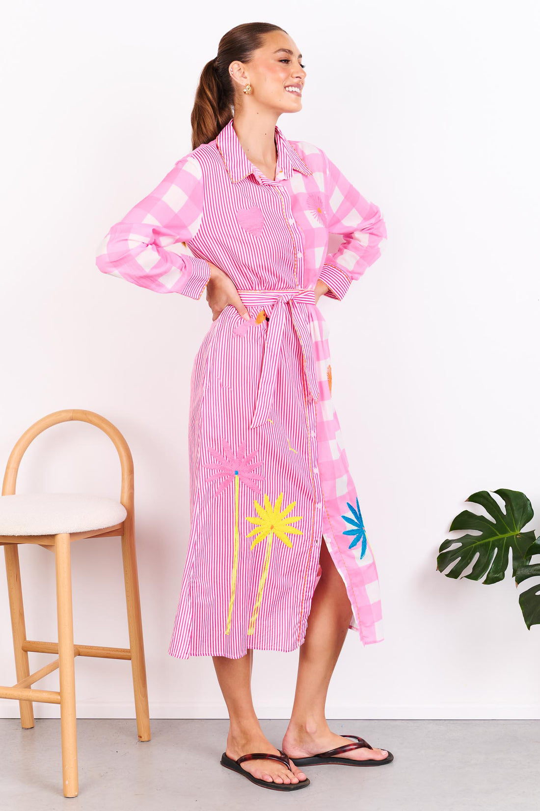 Woman wearing the minnie + MAXXIE Lovely Day Cotton midi shirt dress with long sleeves featuring a pink stripe and gingham print with neon embroidery and a matching waist tie.