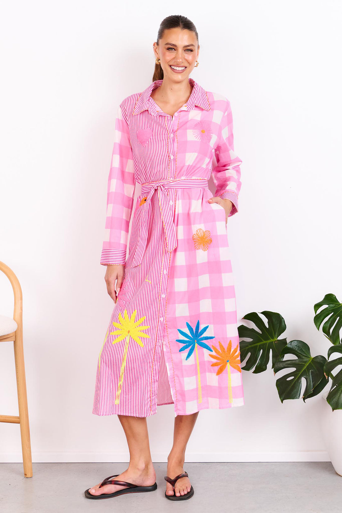 Woman wearing the minnie + MAXXIE Lovely Day Cotton midi shirt dress with long sleeves featuring a pink stripe and gingham print with neon embroidery and a matching waist tie.