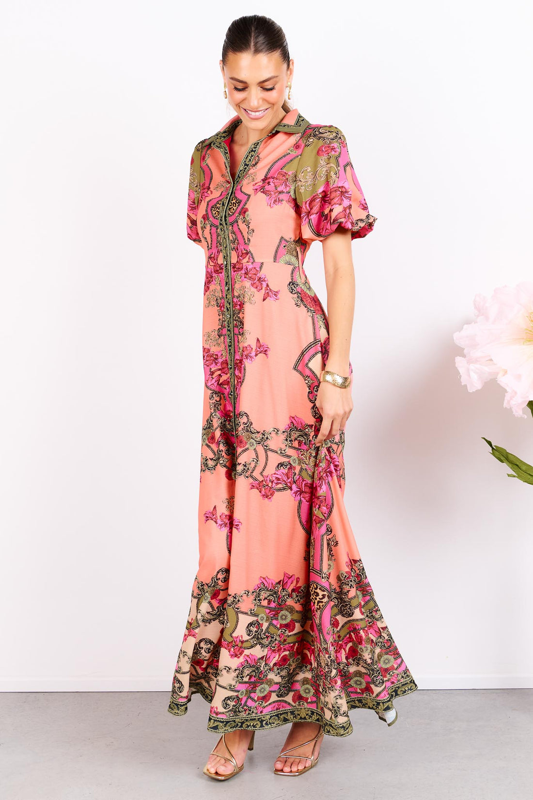 Woman wearing the minnie + MAXXIE Madison Garden peachy pink floral maxi event dress, standing against a white background.