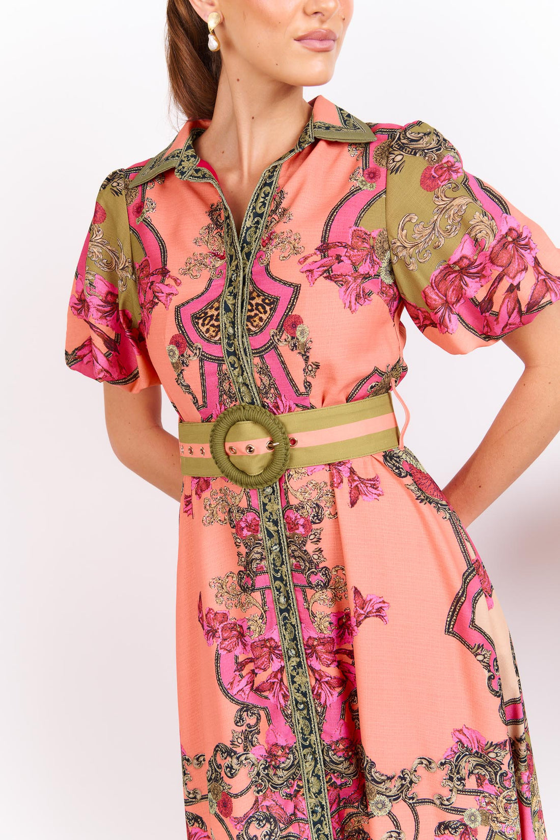 Detail of a woman wearing the minnie + MAXXIE Madison Garden peachy pink floral maxi event dress with a crochet buckle belt, standing against a white background.