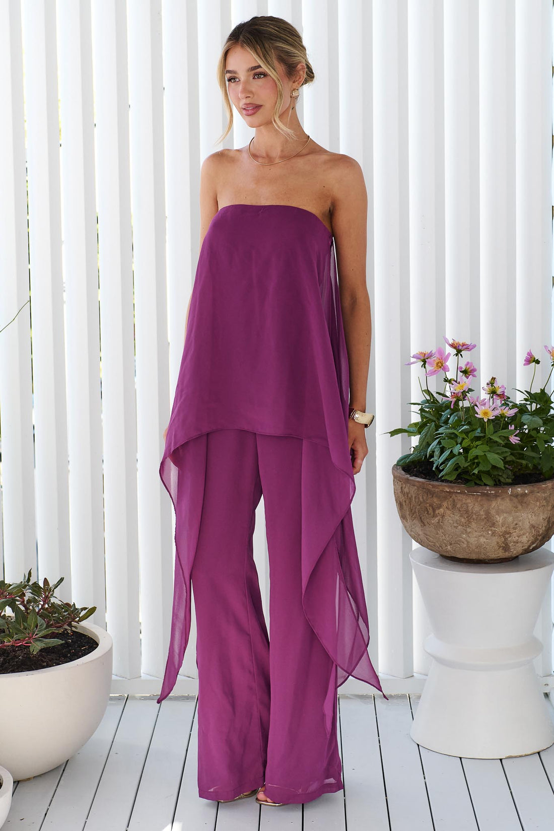A woman wearing the minnie + MAXXIE Margot magenta jumpsuit, with sheer draped side panels.