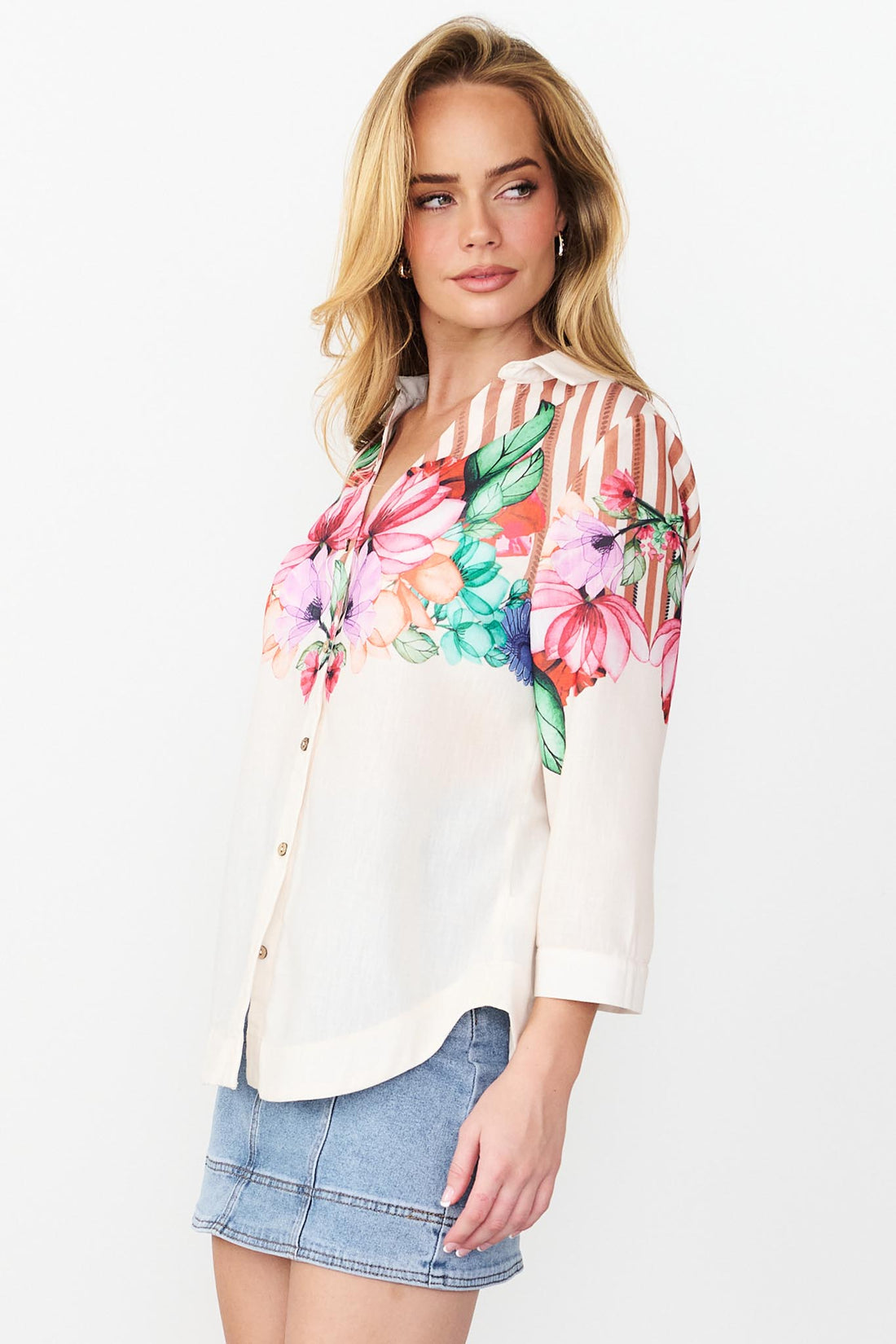 Side view of the Mia Shirt in cinnamon with colourful floral patterns and stripes and a denim skirt