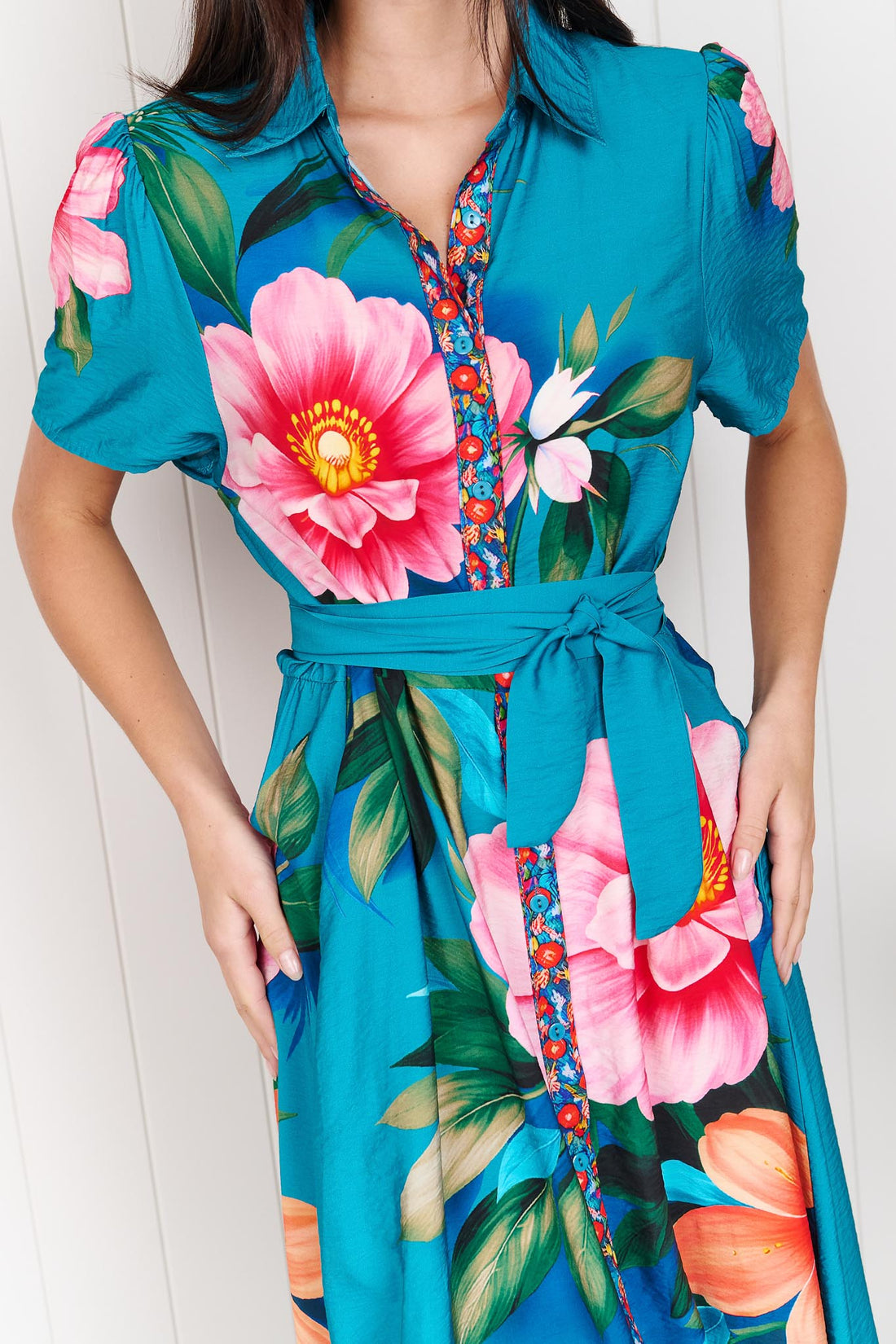 Detail of a woman wearing the minnie + MAXXIE Mona Maxi Dress in bright teal blue with a large floral print and waist tie.