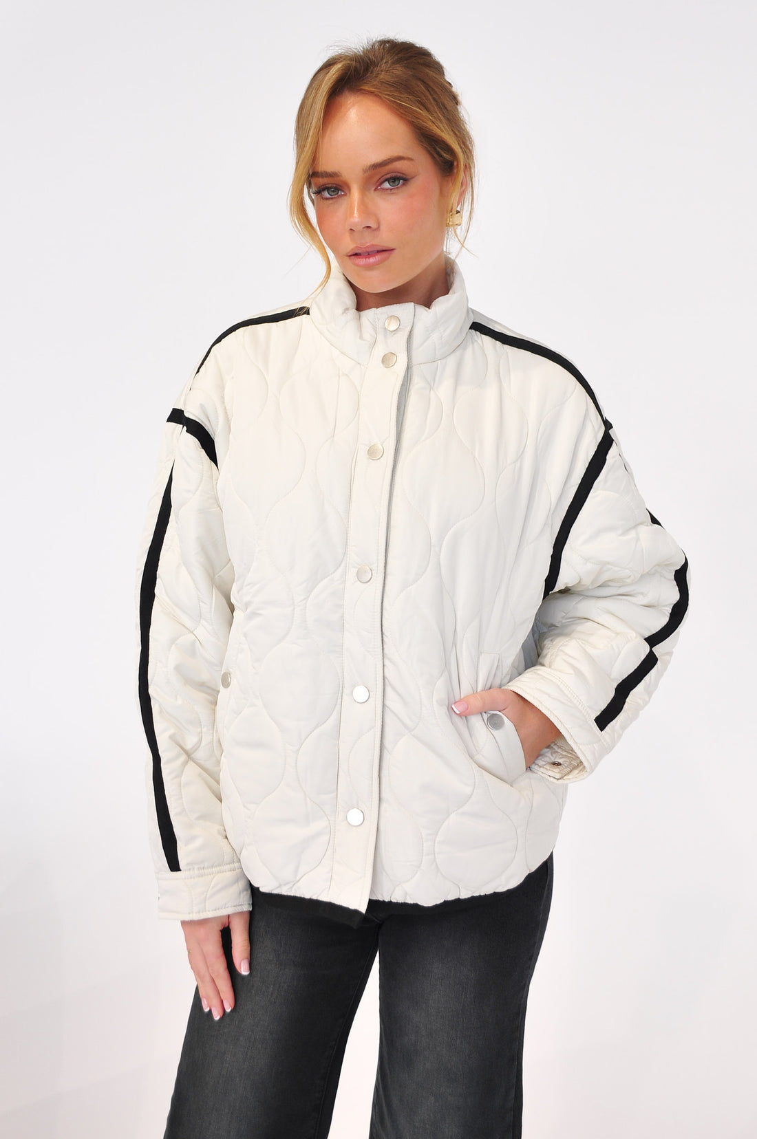Woman wearing a white quilted puffer jacket with black stripes on a white background