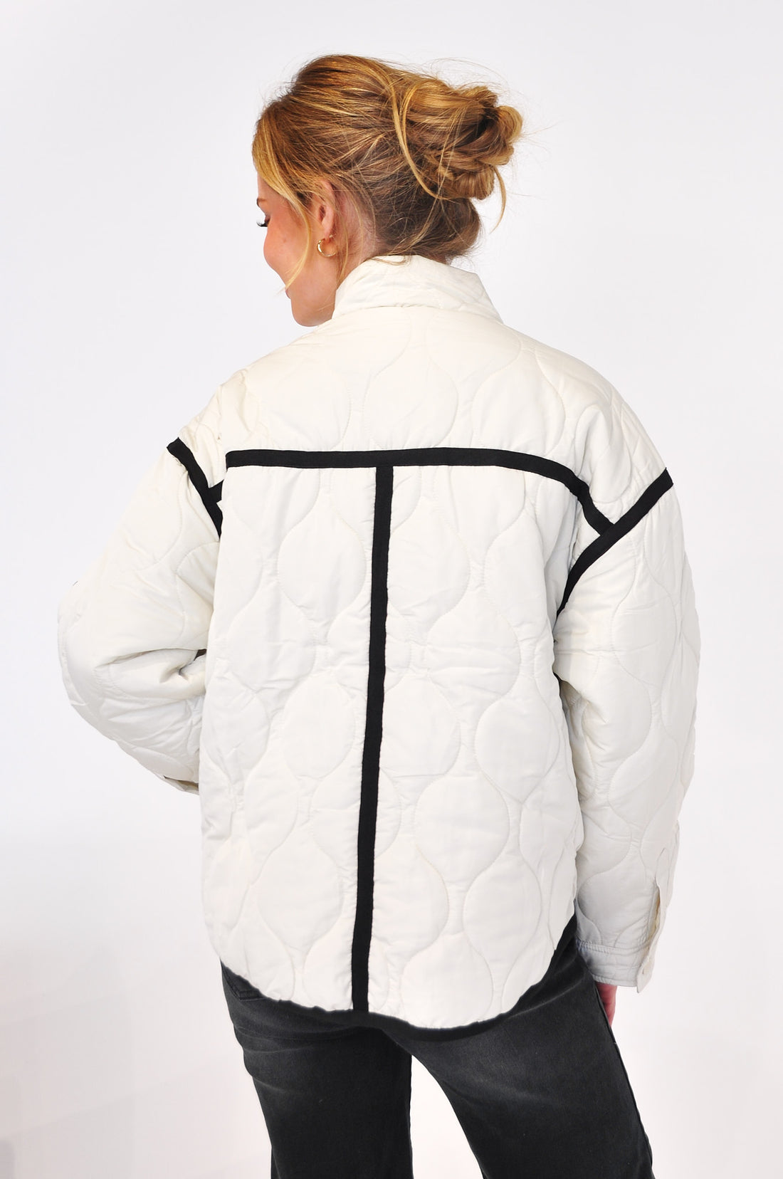 Back view of woman wearing a white quilted puffer jacket with black stripes on a white background