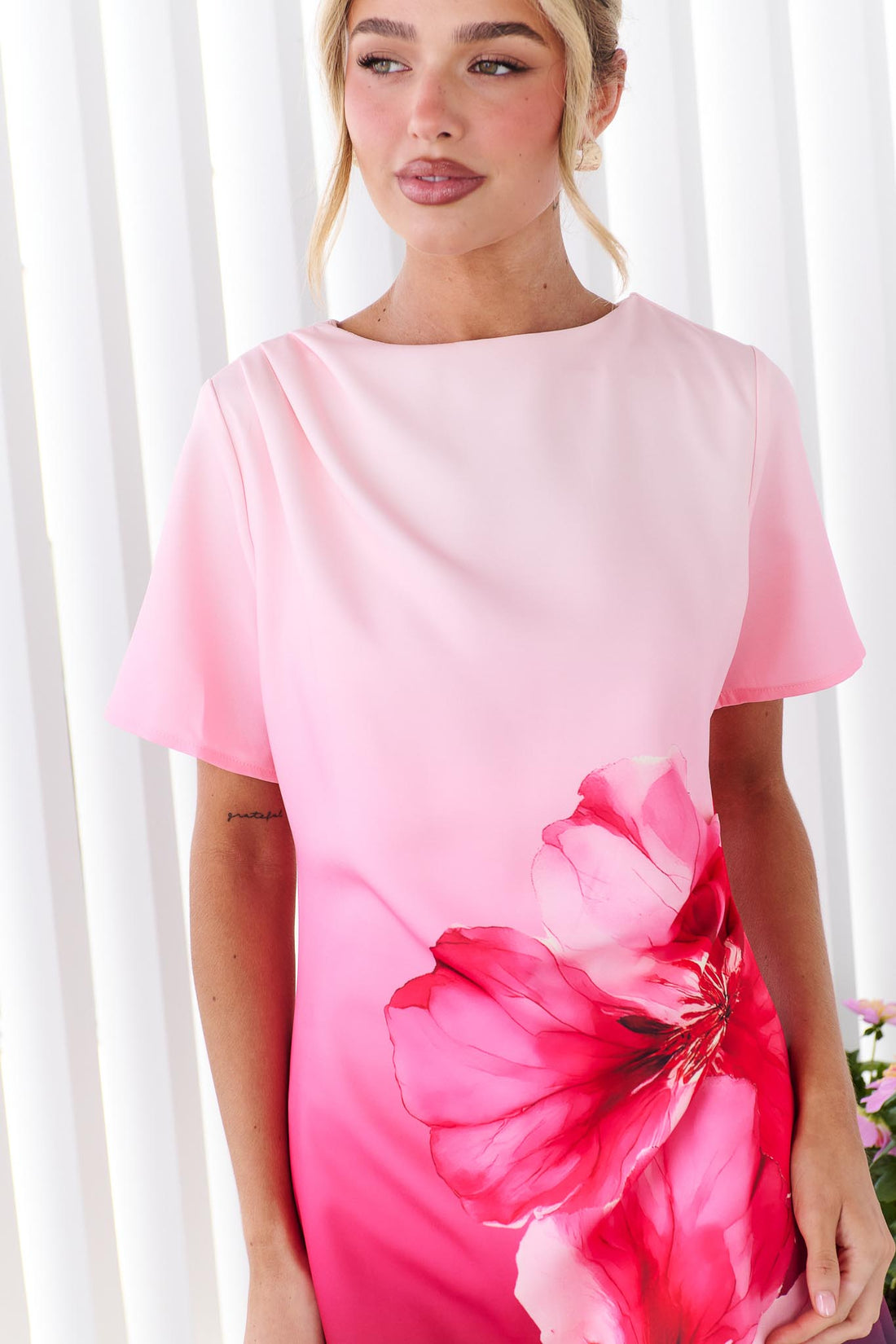 Close up of a woman wearing the minnie + MAXXIE short-sleeve A-line Peony dress with a pink-to-black ombre gradient and a large red hibiscus flower print on the front.