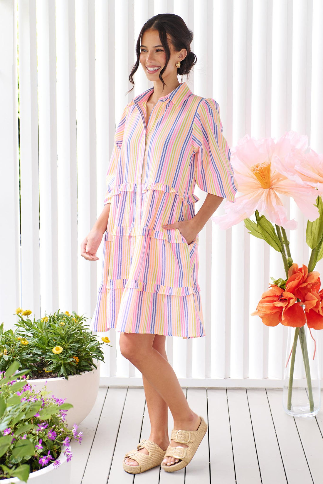 A woman wearing the minnie + MAXXIE Rio A-line short dress with elbow length sleeves, a tiered shape and a colourful neon stripe print.