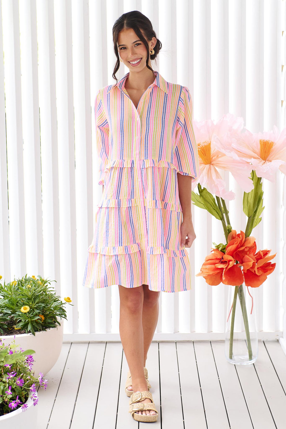 A woman wearing the minnie + MAXXIE Rio A-line short dress with elbow length sleeves, a tiered shape and a colourful neon stripe print.