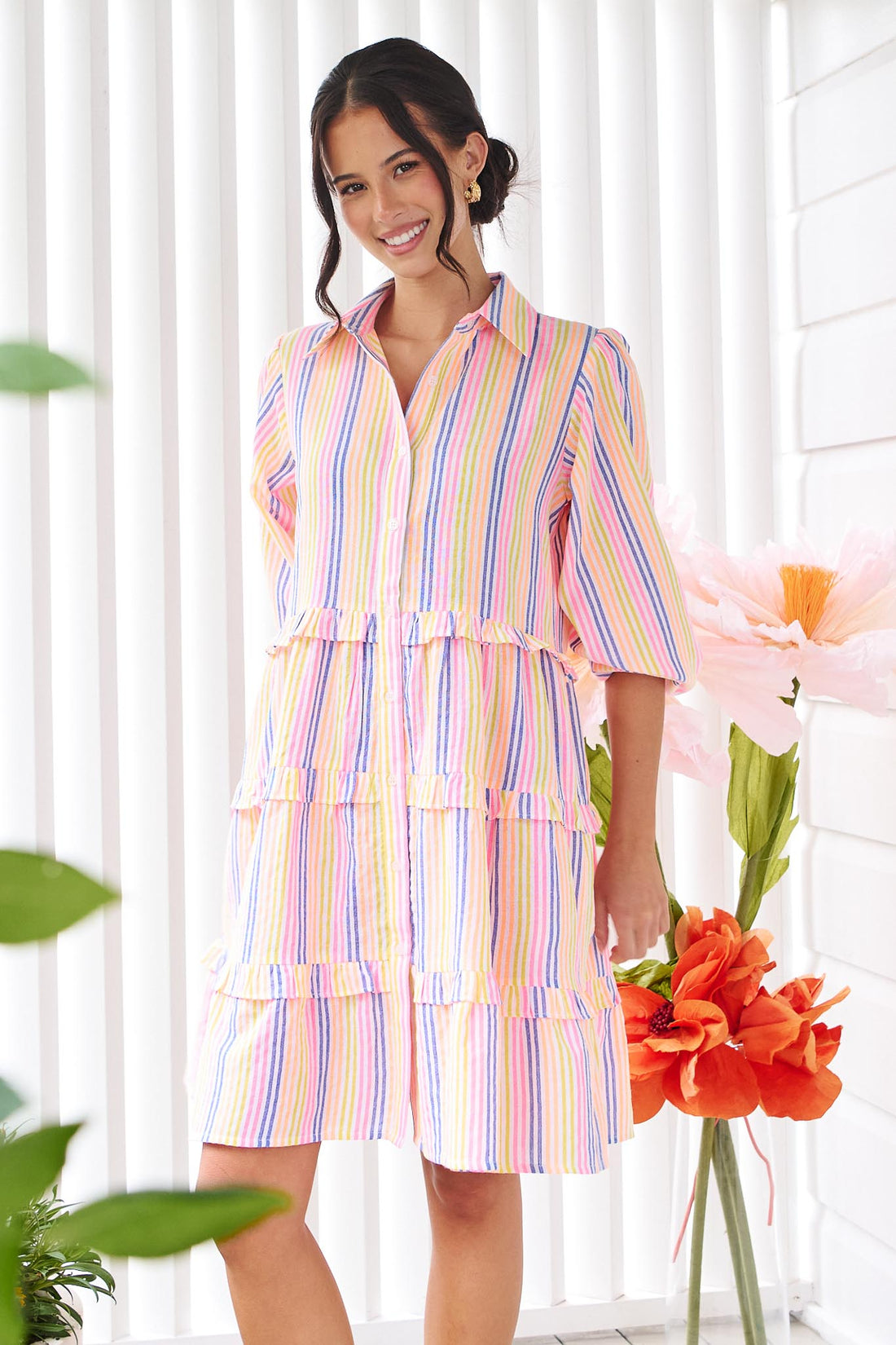 A woman wearing the minnie + MAXXIE Rio A-line short dress with elbow length sleeves, a tiered shape and a colourful neon stripe print.