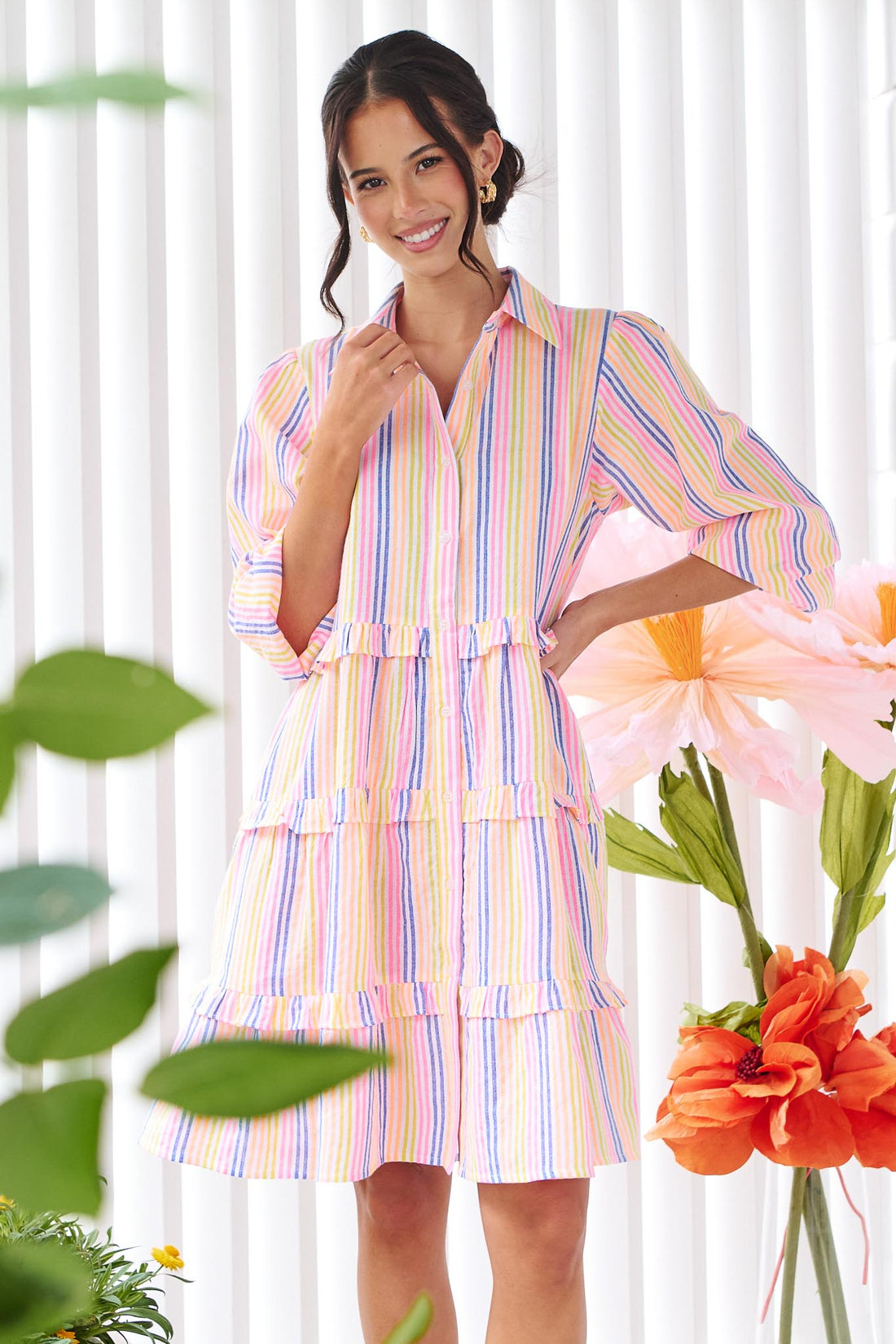 A woman wearing the minnie + MAXXIE Rio A-line short dress with elbow length sleeves, a tiered shape and a colourful neon stripe print.