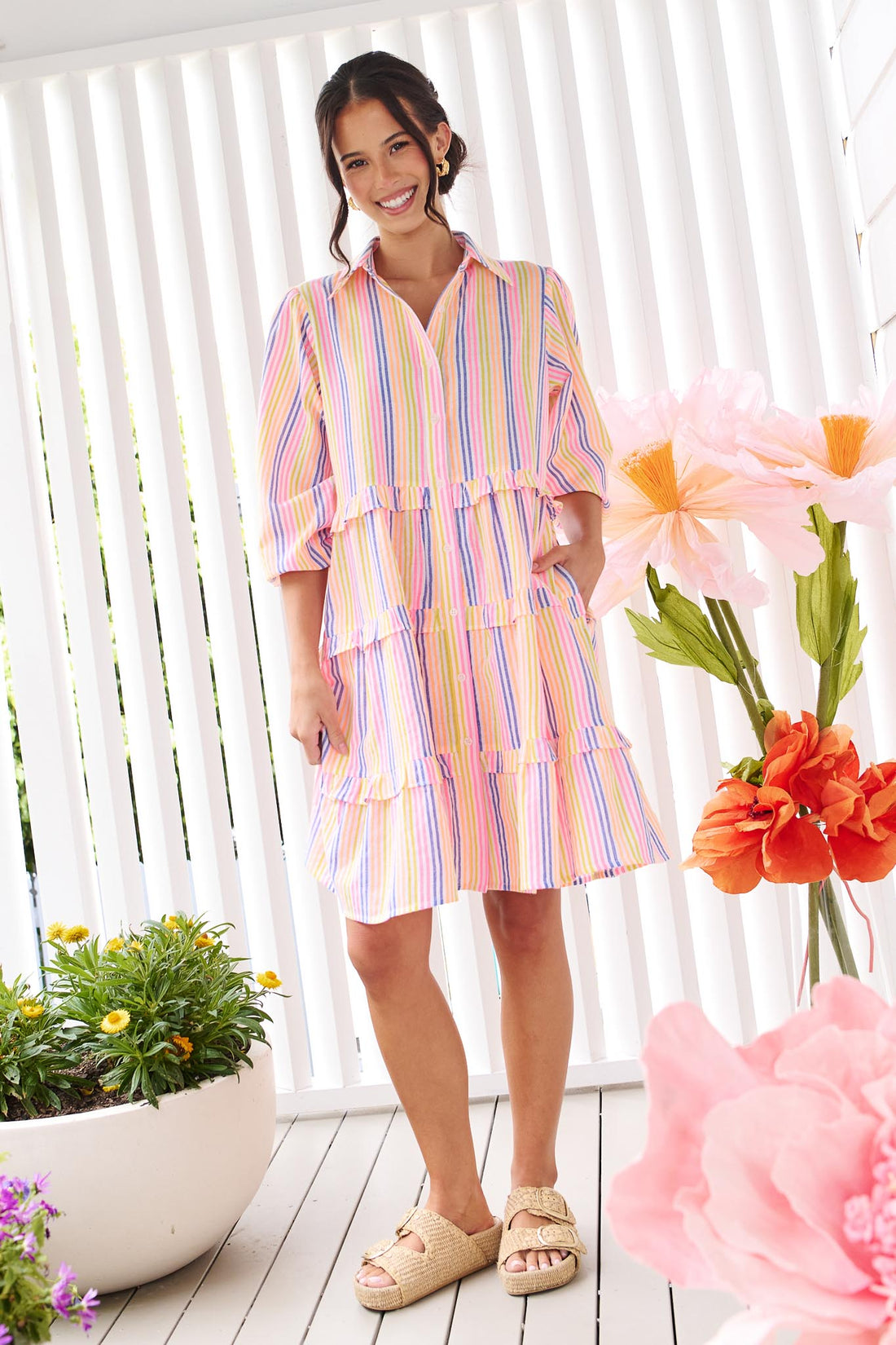 A woman wearing the minnie + MAXXIE Rio A-line short dress with elbow length sleeves, a tiered shape and a colourful neon stripe print.