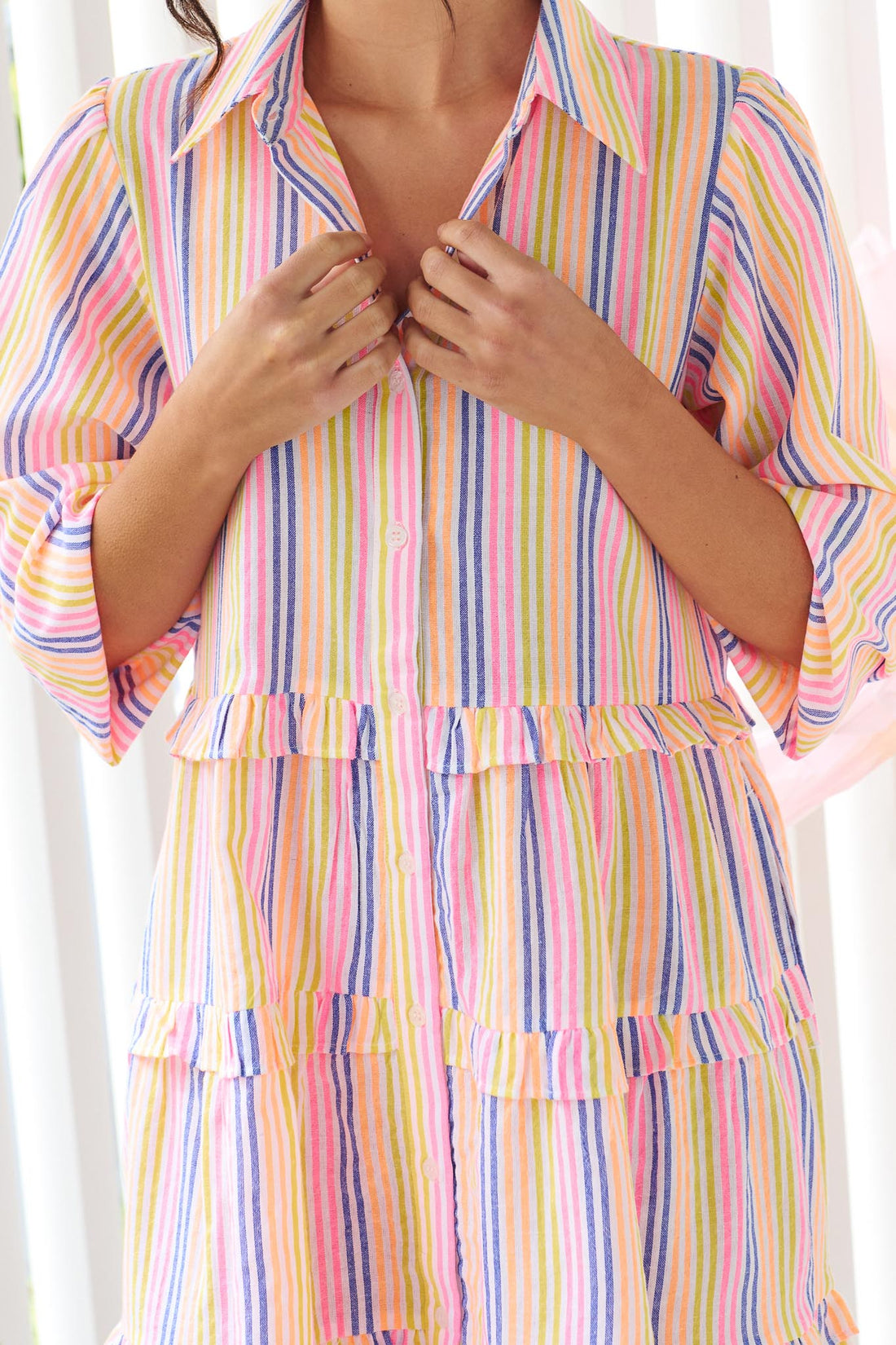 Detail of a woman wearing the minnie + MAXXIE Rio A-line short dress with elbow length sleeves, a tiered shape and a colourful neon stripe print.