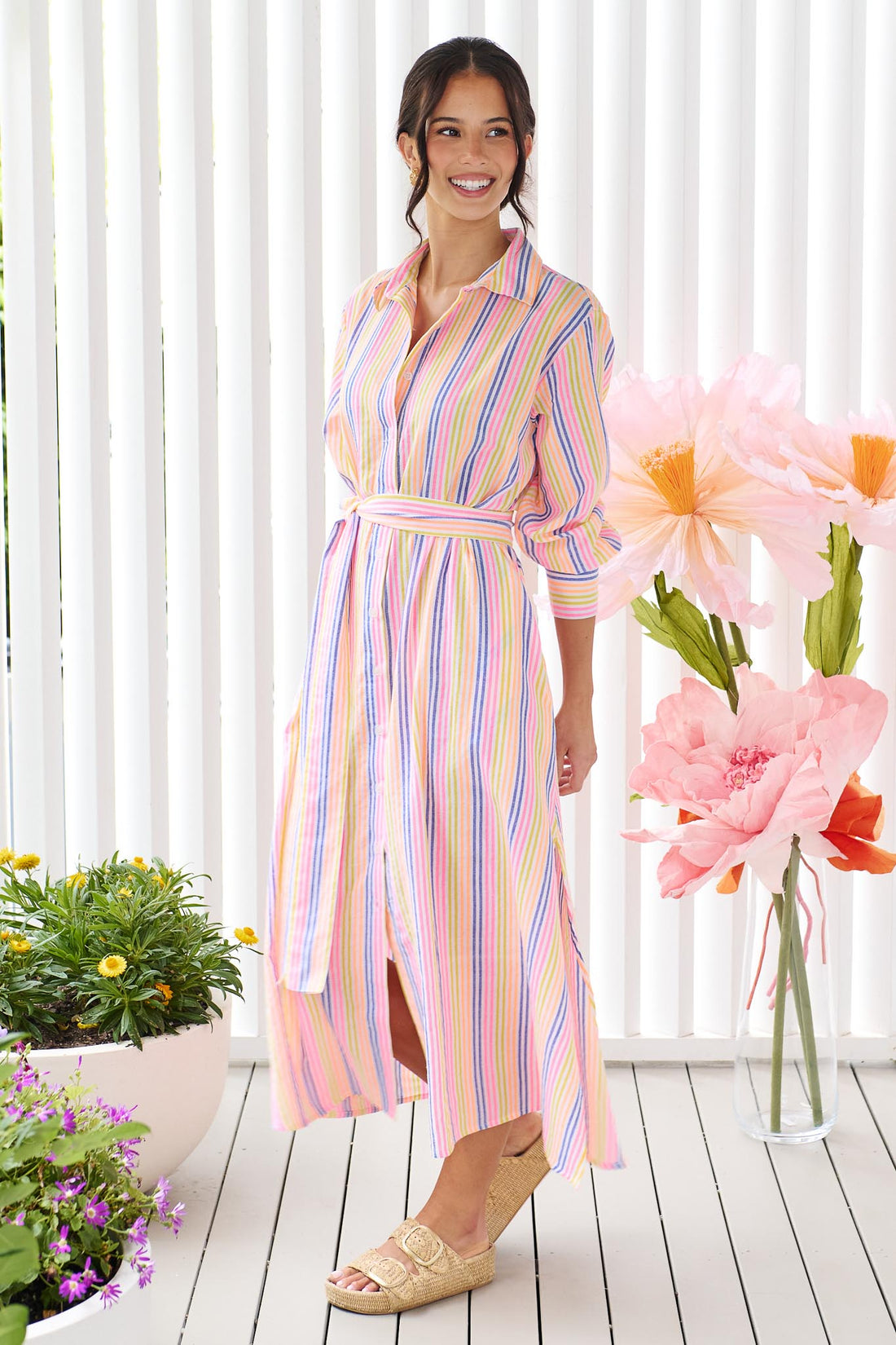 A woman wearing the minnie + MAXXIE Rio midi dress with 3/4 sleeves, colourful neon stripe print and a tie at the waist.