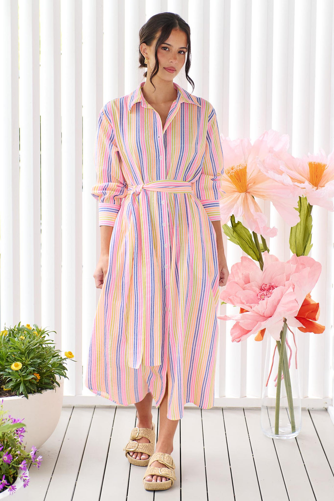 A woman wearing the minnie + MAXXIE Rio midi dress with 3/4 sleeves, colourful neon stripe print and a tie at the waist.