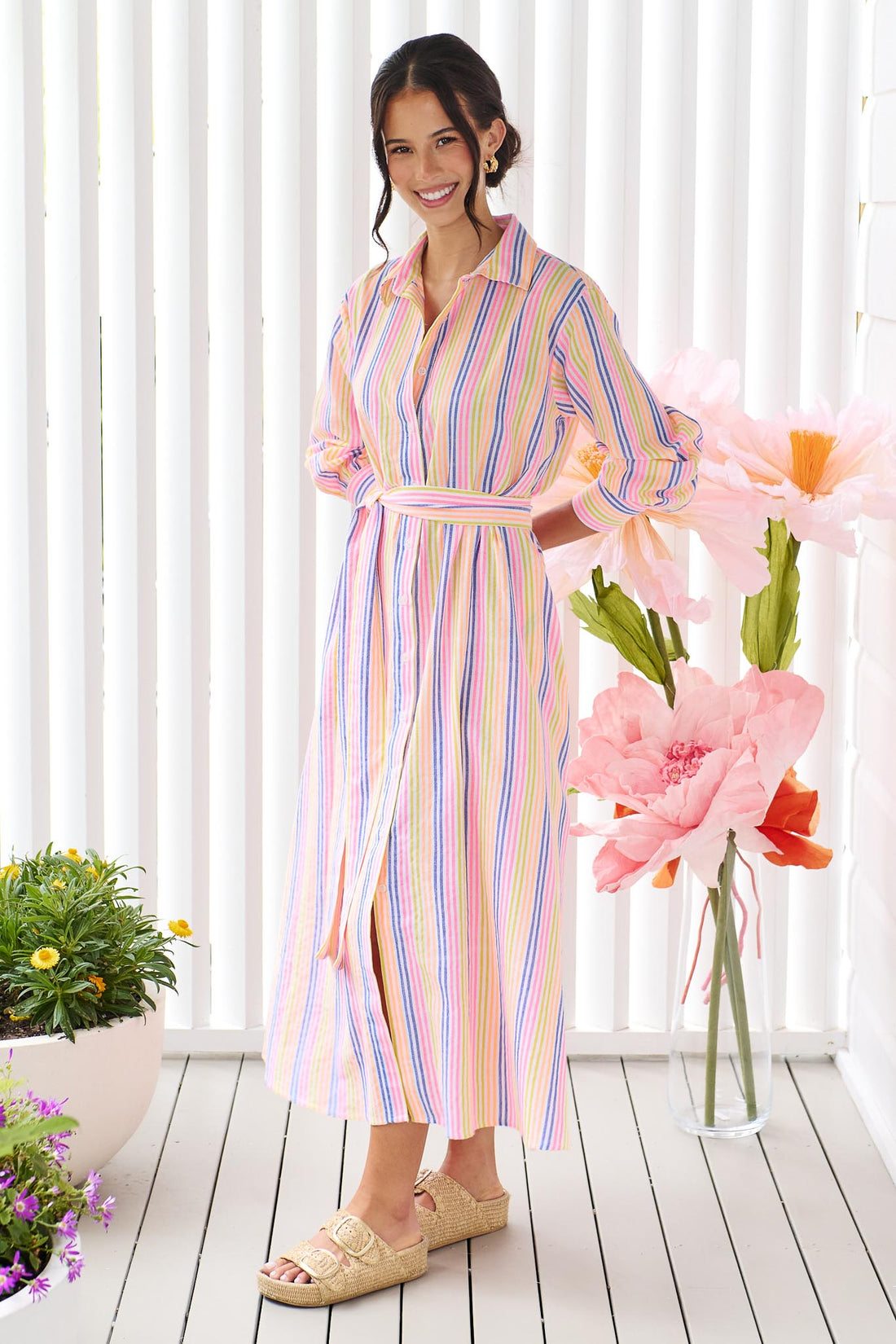 A woman wearing the minnie + MAXXIE Rio midi dress with 3/4 sleeves, colourful neon stripe print and a tie at the waist.