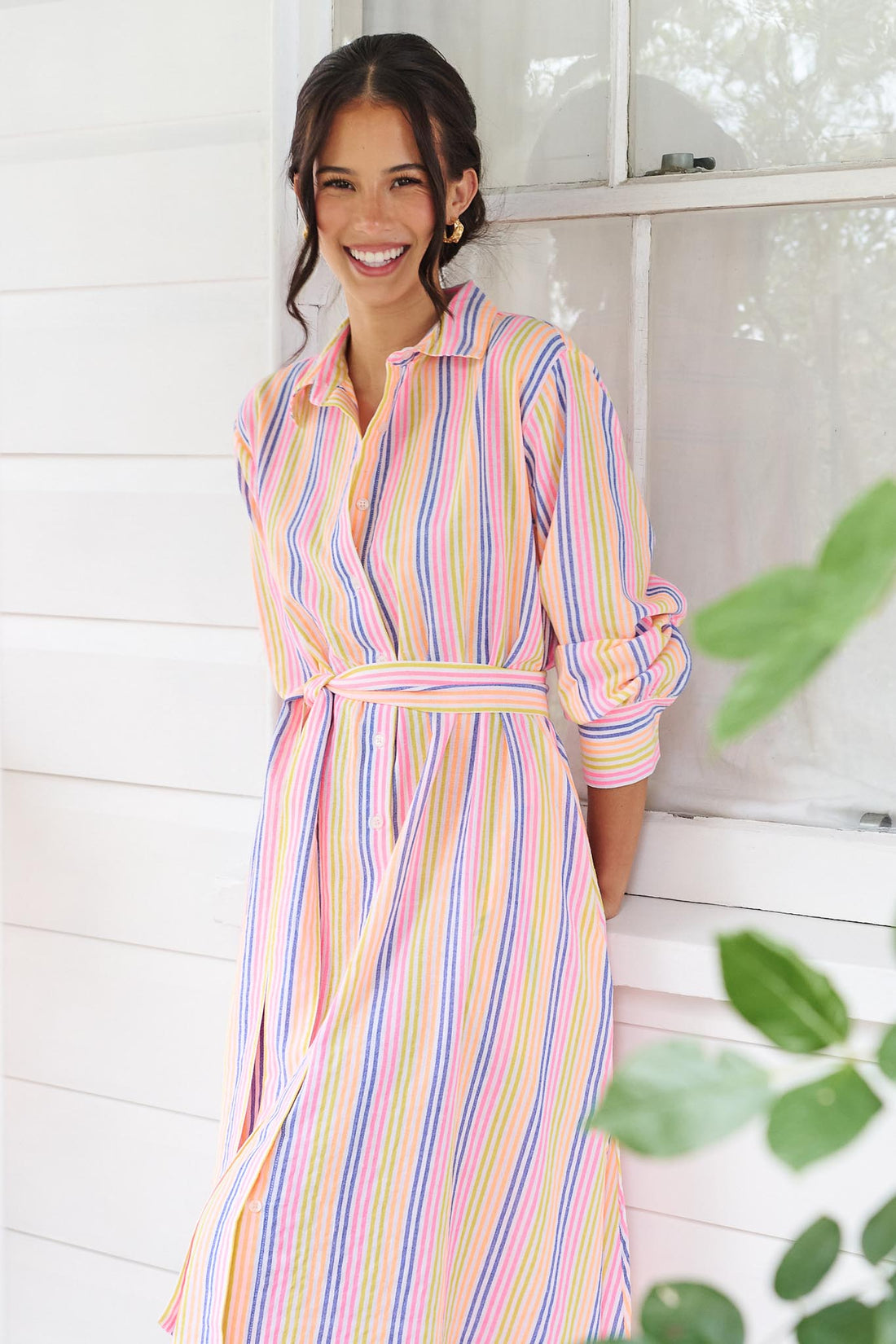 A woman wearing the minnie + MAXXIE Rio midi dress with 3/4 sleeves, colourful neon stripe print and a tie at the waist.