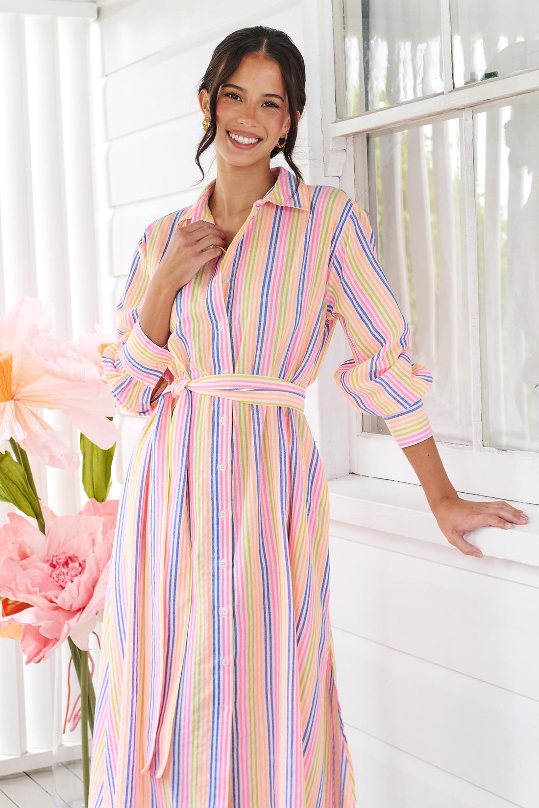 A woman wearing the minnie + MAXXIE Rio midi dress with 3/4 sleeves, colourful neon stripe print and a tie at the waist.