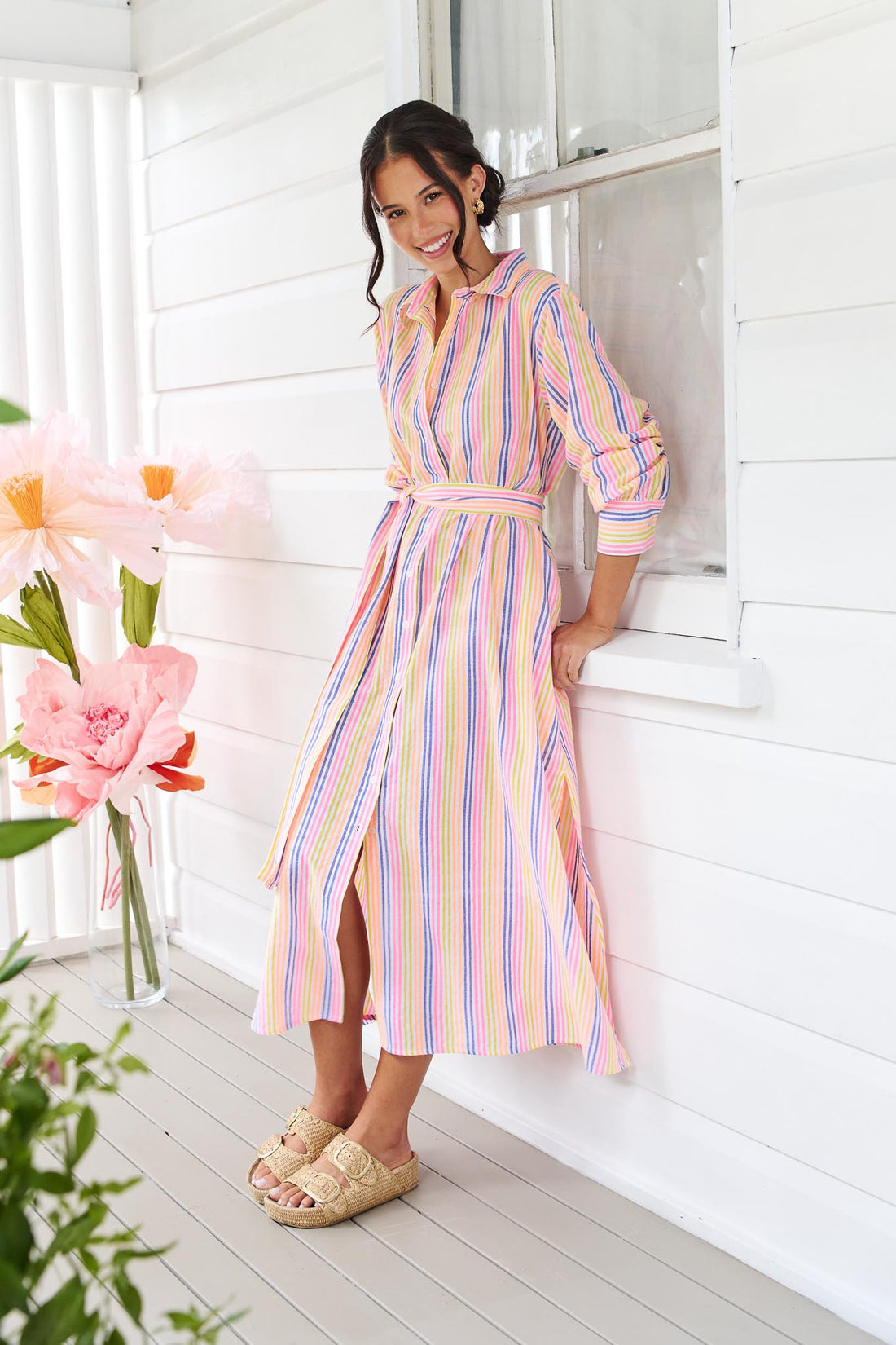A woman wearing the minnie + MAXXIE Rio midi dress with 3/4 sleeves, colourful neon stripe print and a tie at the waist.