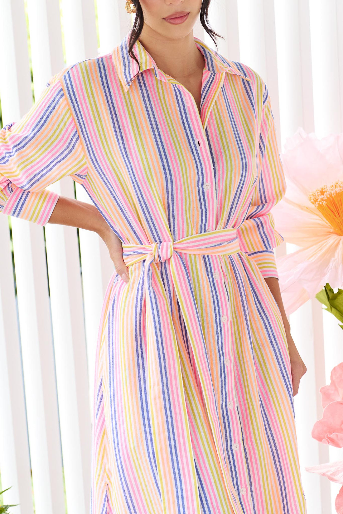 Close up of a woman wearing the minnie + MAXXIE Rio midi dress with 3/4 sleeves, colourful neon stripe print and a tie at the waist.